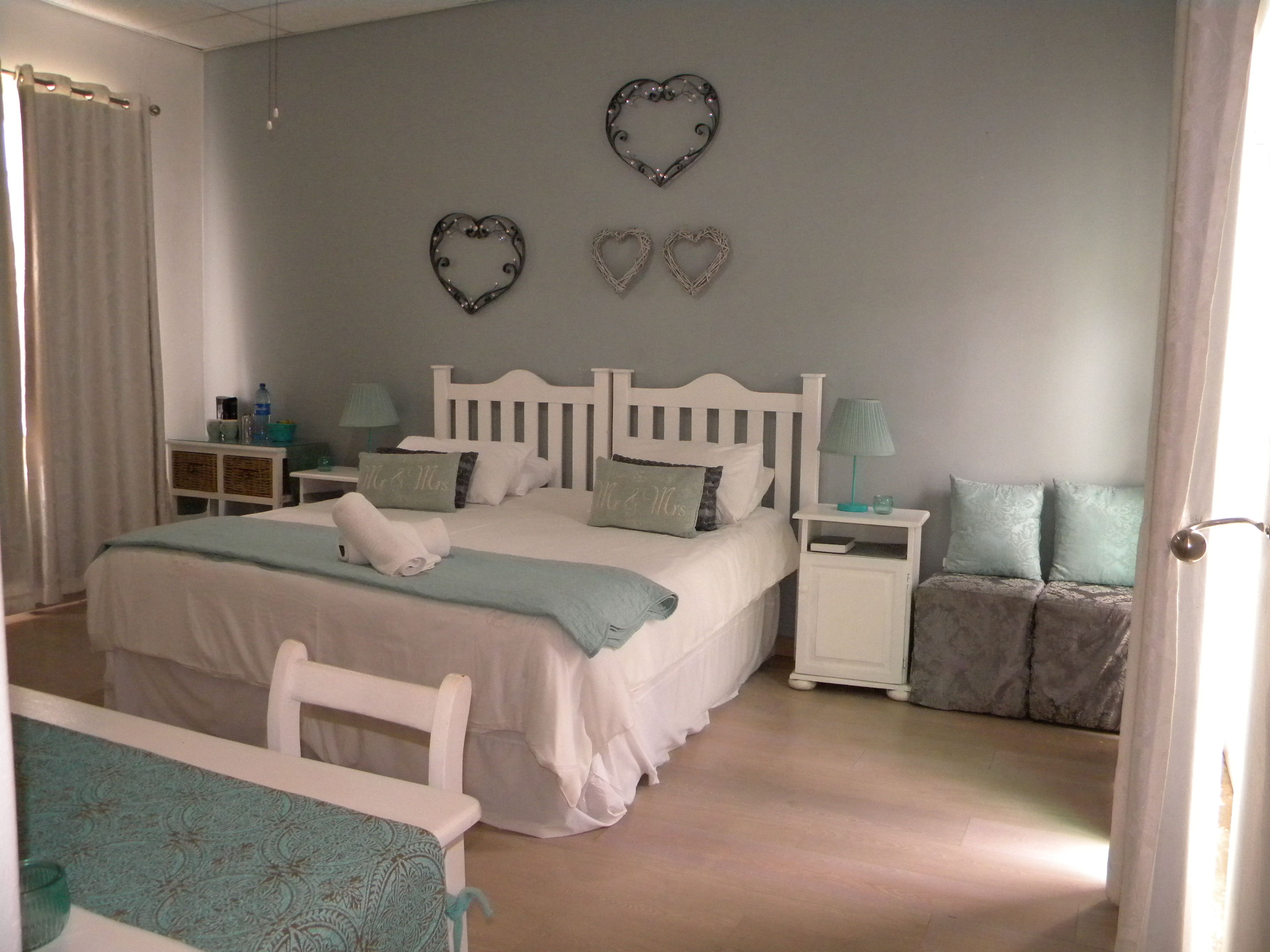 Un dormitorio con una cama blanca, dos mesitas de noche, una silla blanca y una puerta.