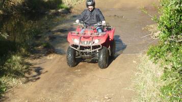 Una persona guida un quad rosso su un sentiero sterrato circondato dal verde.