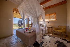 A bedroom with a bed, a fan, a chair, and a cowhide rug. - De Zeekoe Guest Farm (Oudtshoorn)