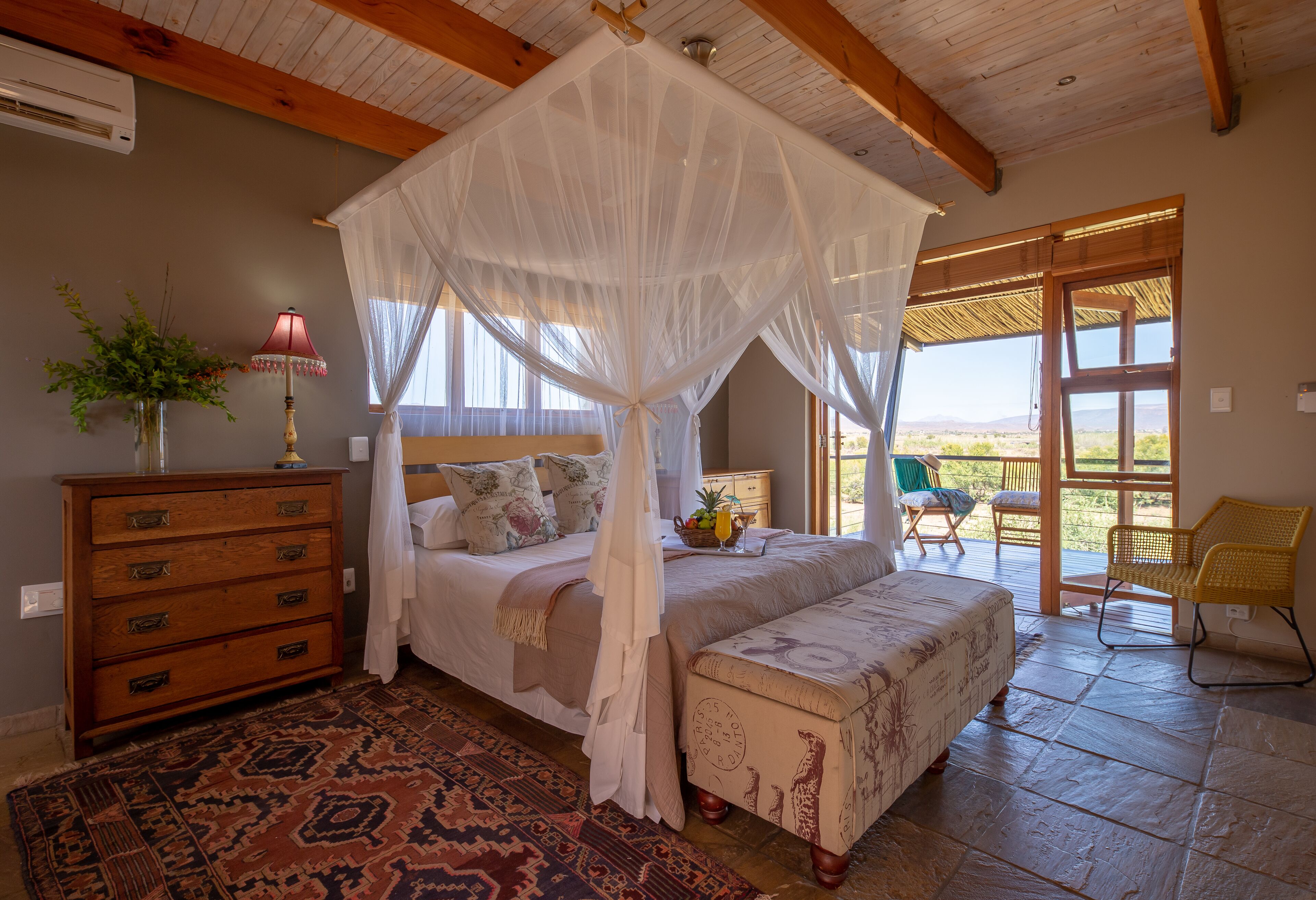 A bedroom with a canopy bed, a wooden dresser, a patterned rug, and a view of the outdoors through a glass door.