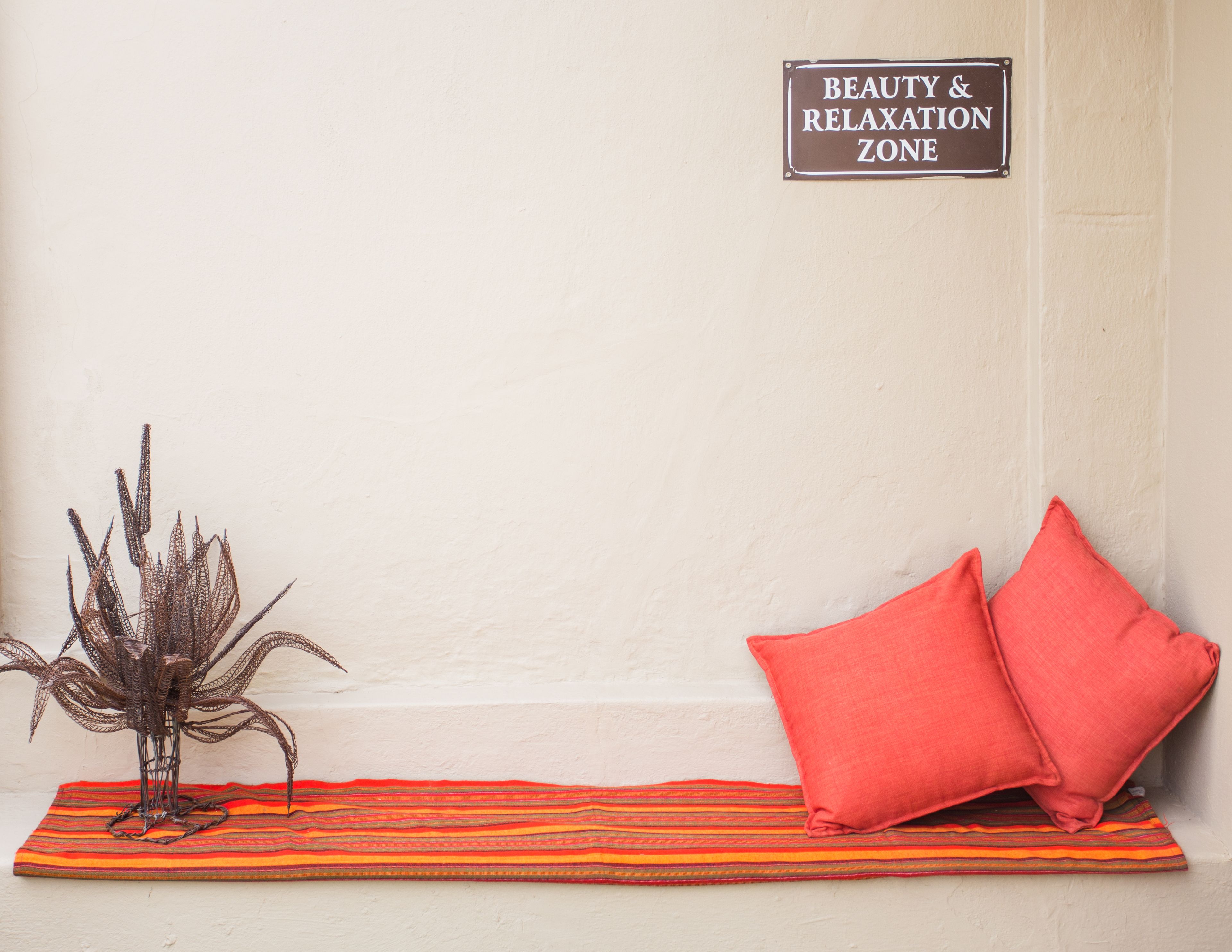 A corner with a sign reading "Beauty & Relaxation Zone," a striped rug, a red pillow, and a decorative plant.