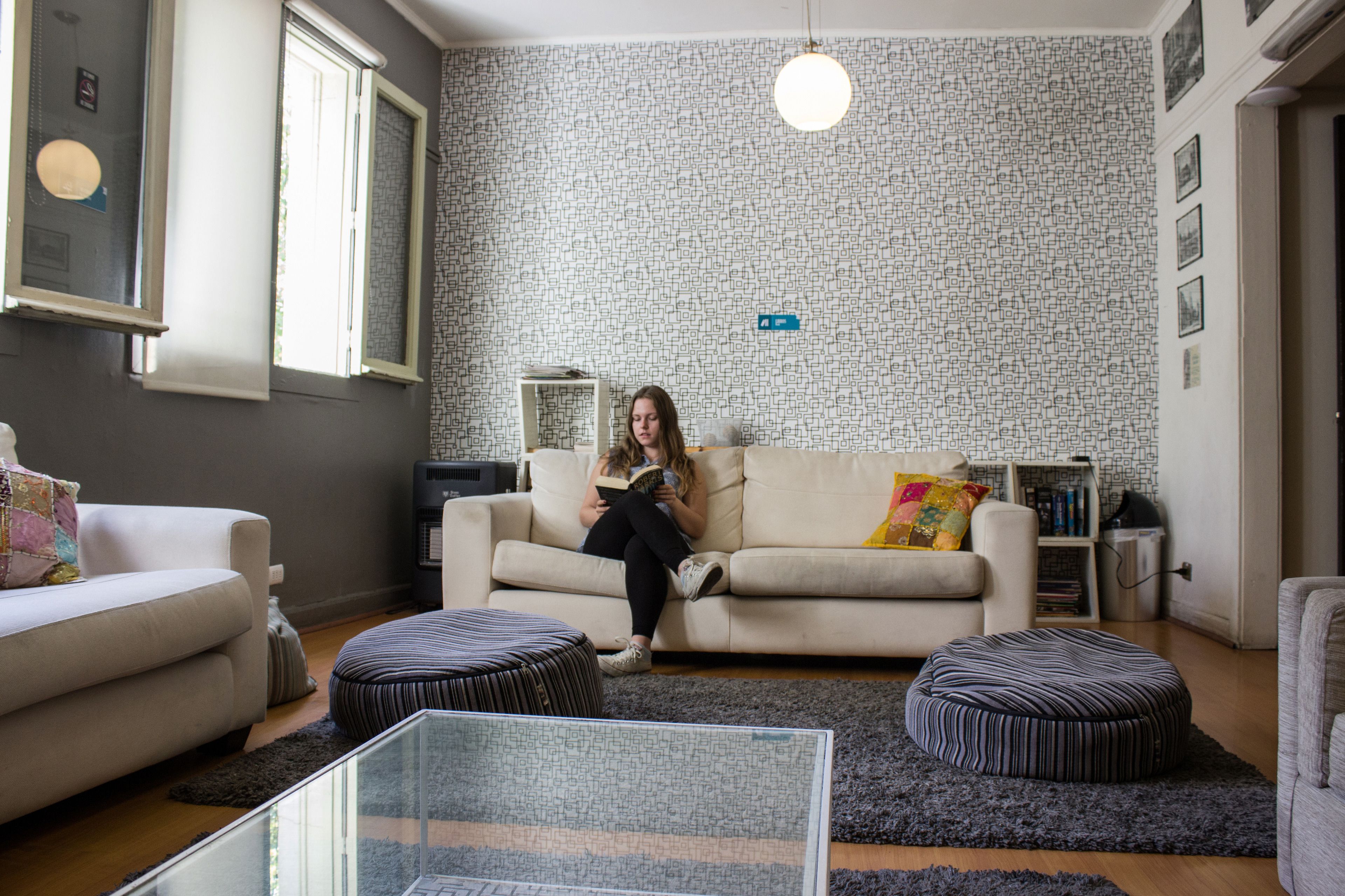 Een woonkamer met een bank, poefs, een glazen salontafel en een behang met een patroon.