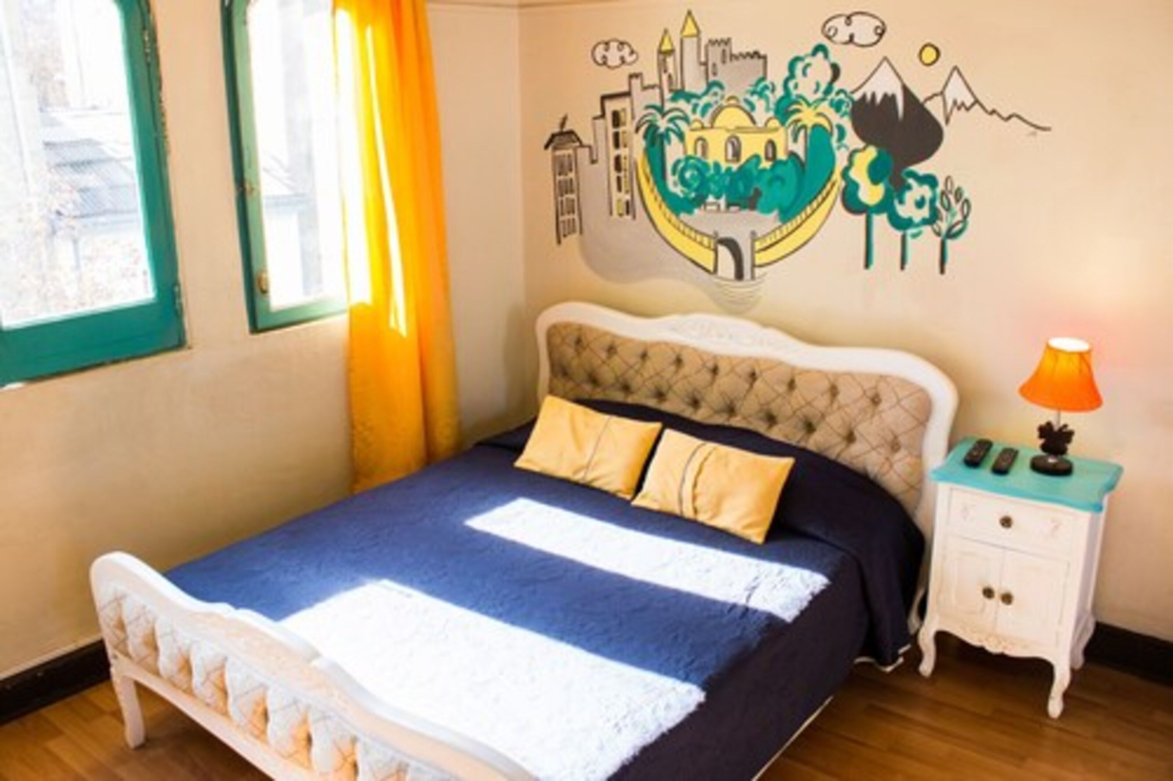 A bedroom with a bed, a nightstand, a lamp, and a wall mural.