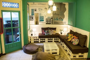 A cozy room with a green wall, a sofa, a small table, and a bench. - Hostal Forestal - Hostel (Santiago)