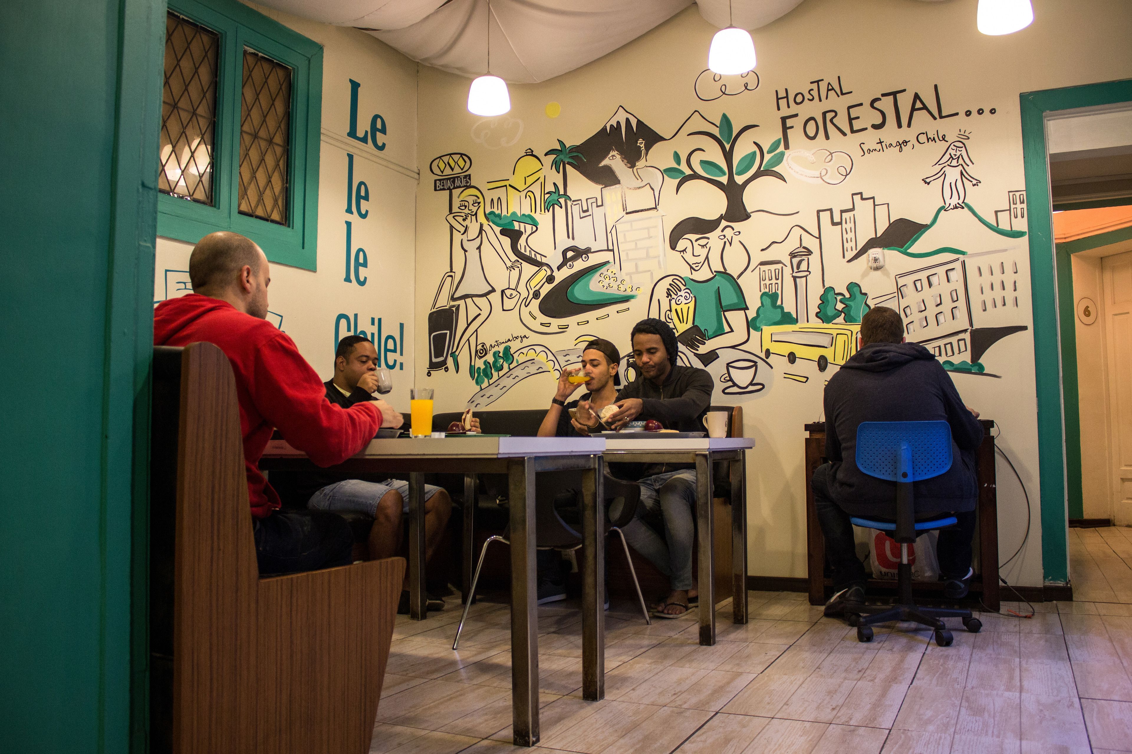 A group of people sitting around a table in a room with a mural depicting a cityscape and a tree.