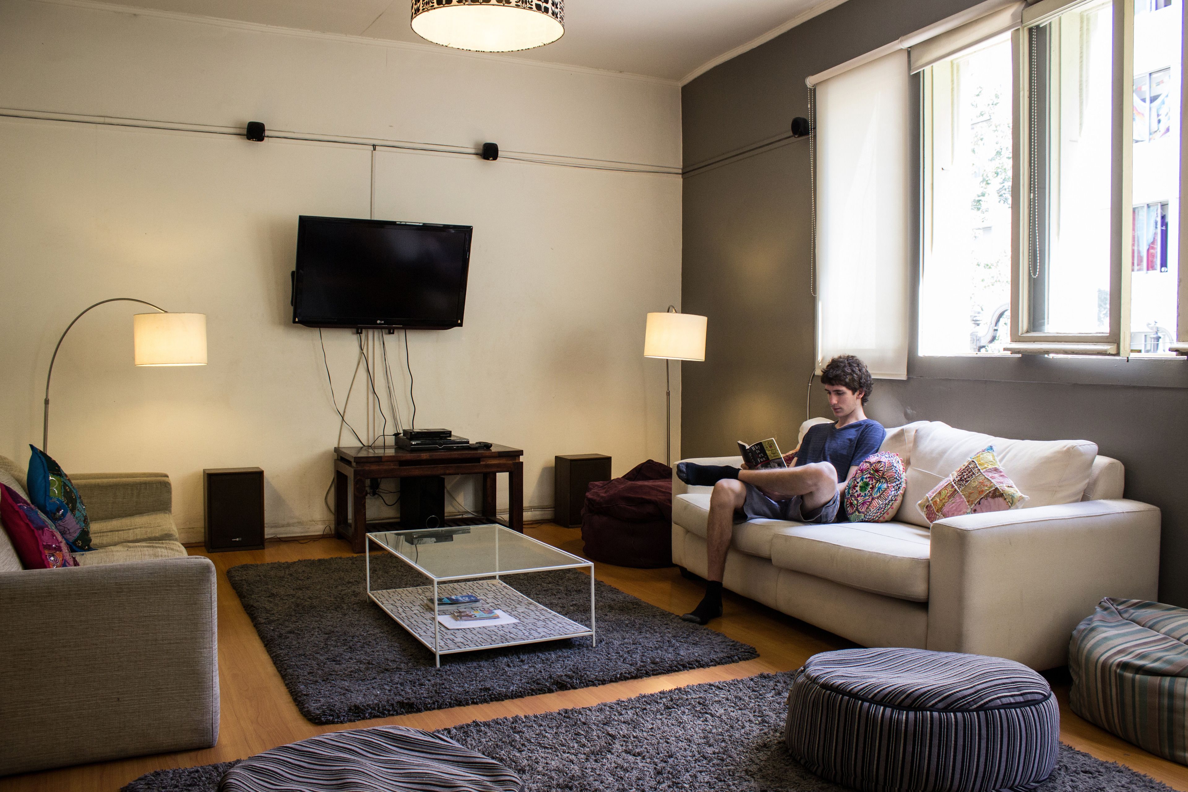 Una sala de estar con una televisión de pantalla plana, dos lámparas, una mesa de centro, un sofá y una ventana con persianas.