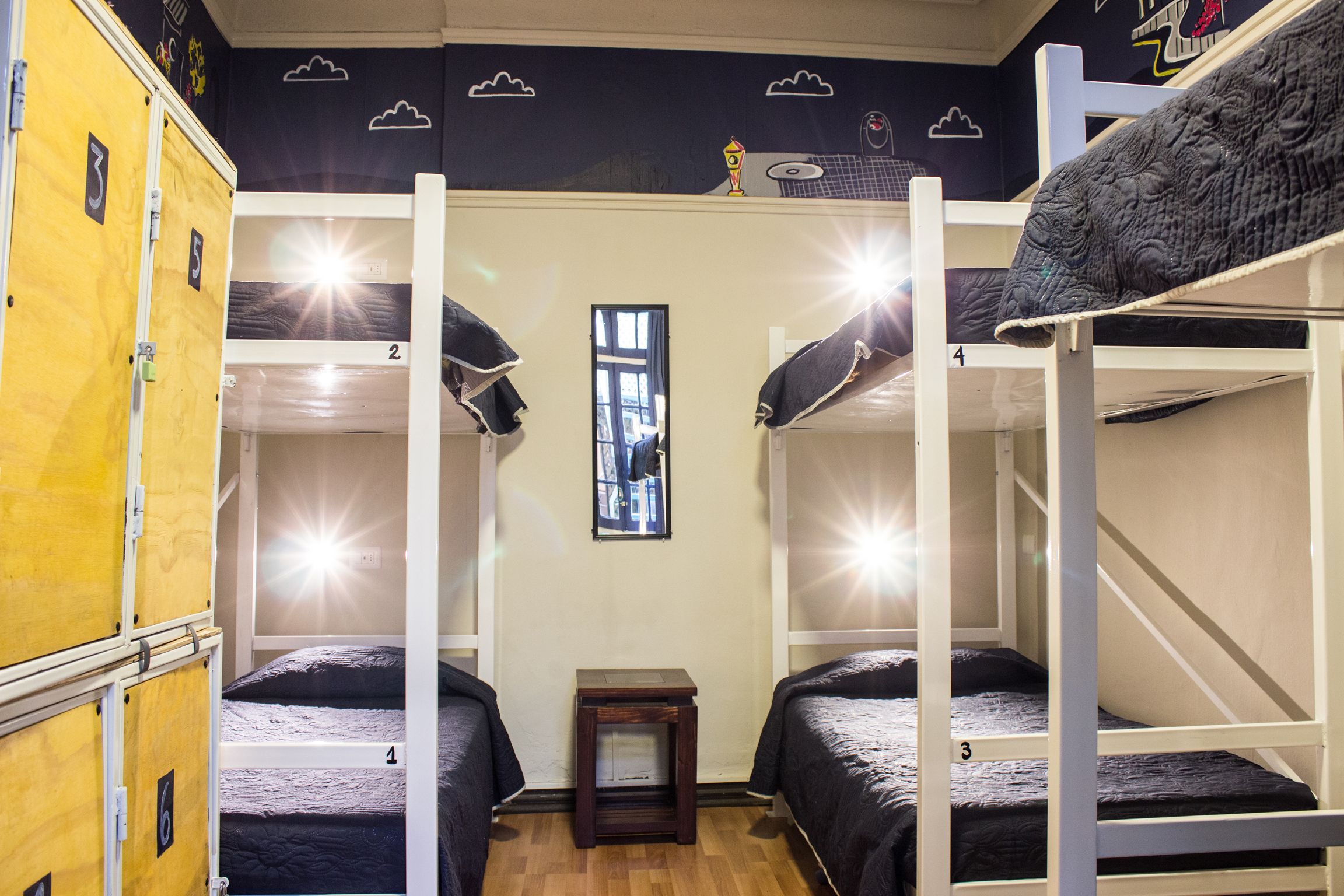 A bunk bed room with bunk numbers 2, 3, and 4, a small wooden nightstand, and a window with a view of the city.
