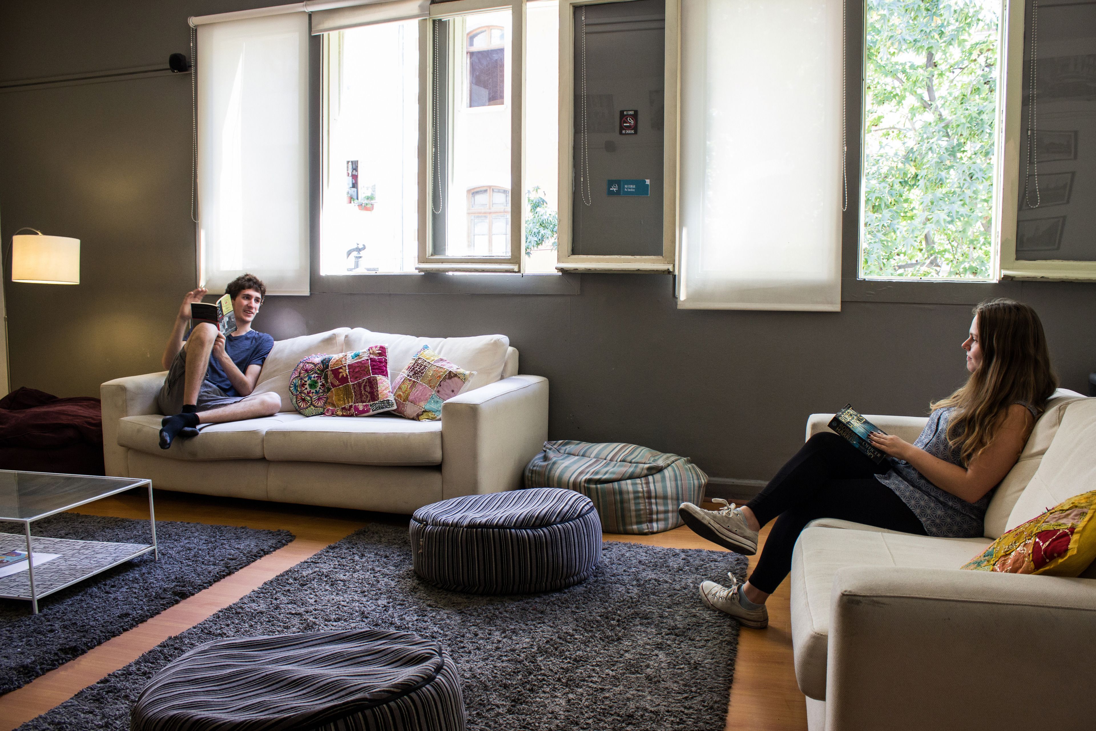 A living room with a sofa, ottomans, and a coffee table. There are windows with blinds and a lamp on a table.