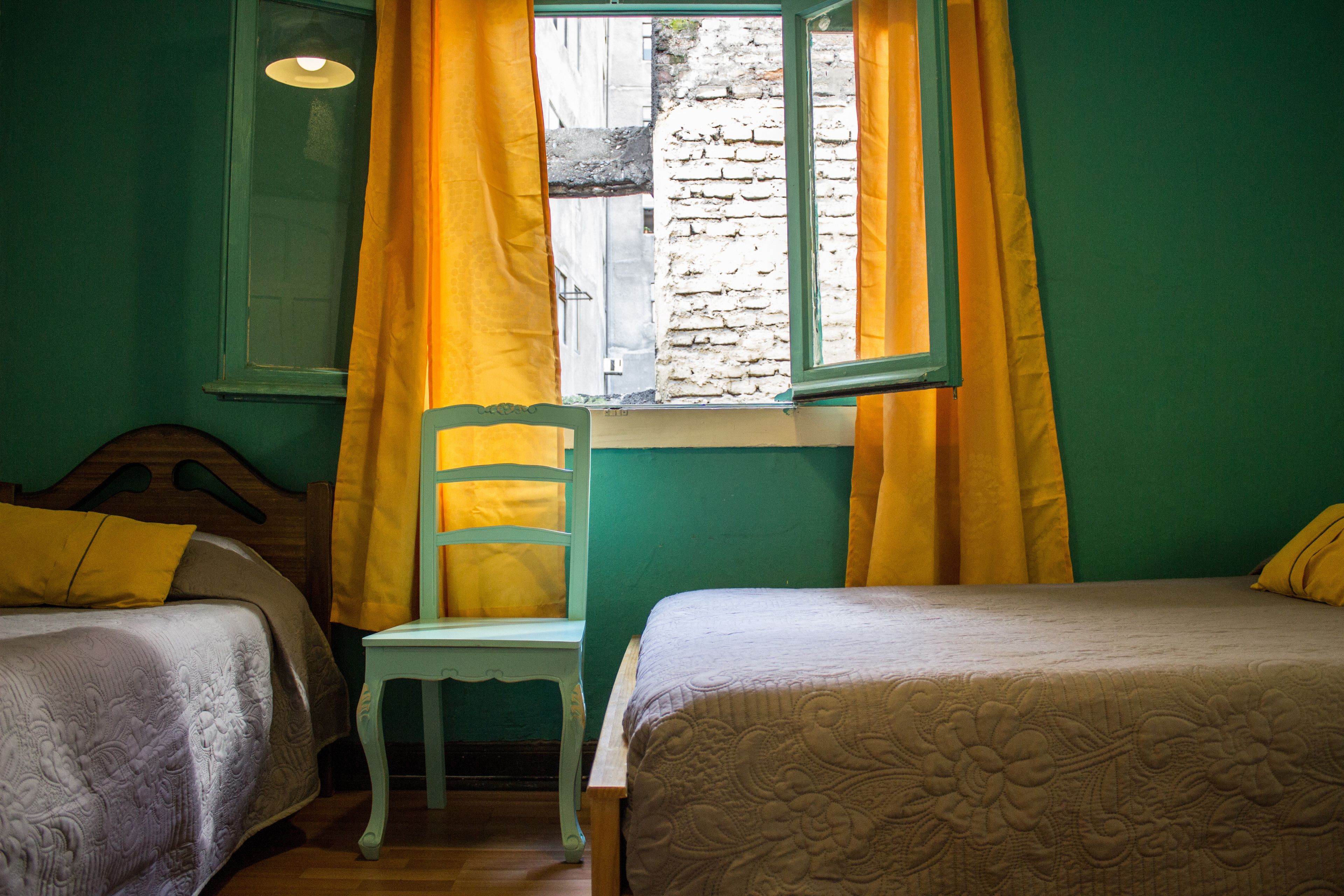 A room with two beds, a chair, and a window with yellow curtains.