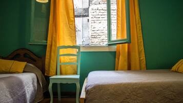 A room with two beds, a chair, and a window with yellow curtains.