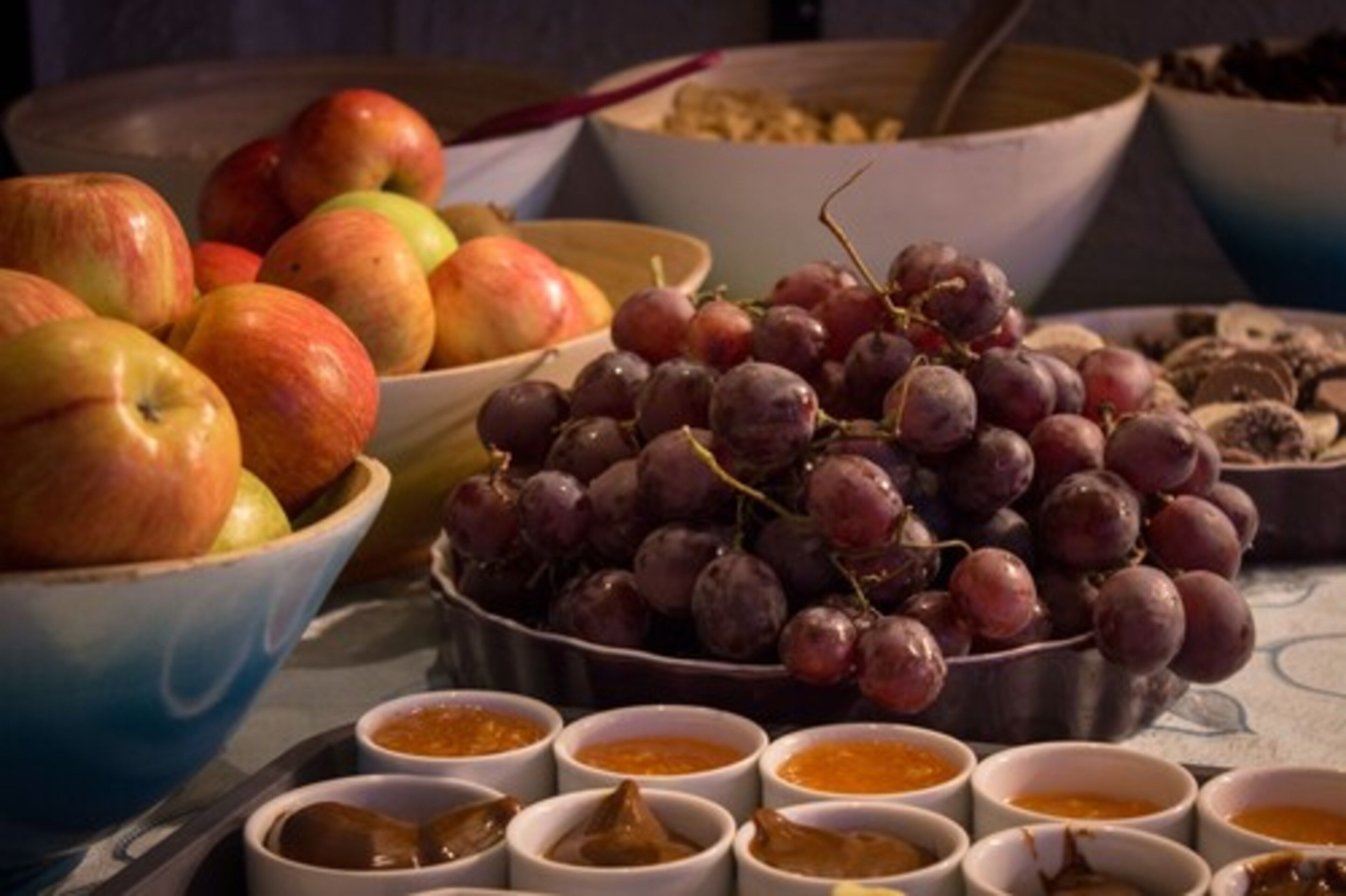 Una mesa con tazones de manzanas, uvas y pequeños recipientes de salsas.