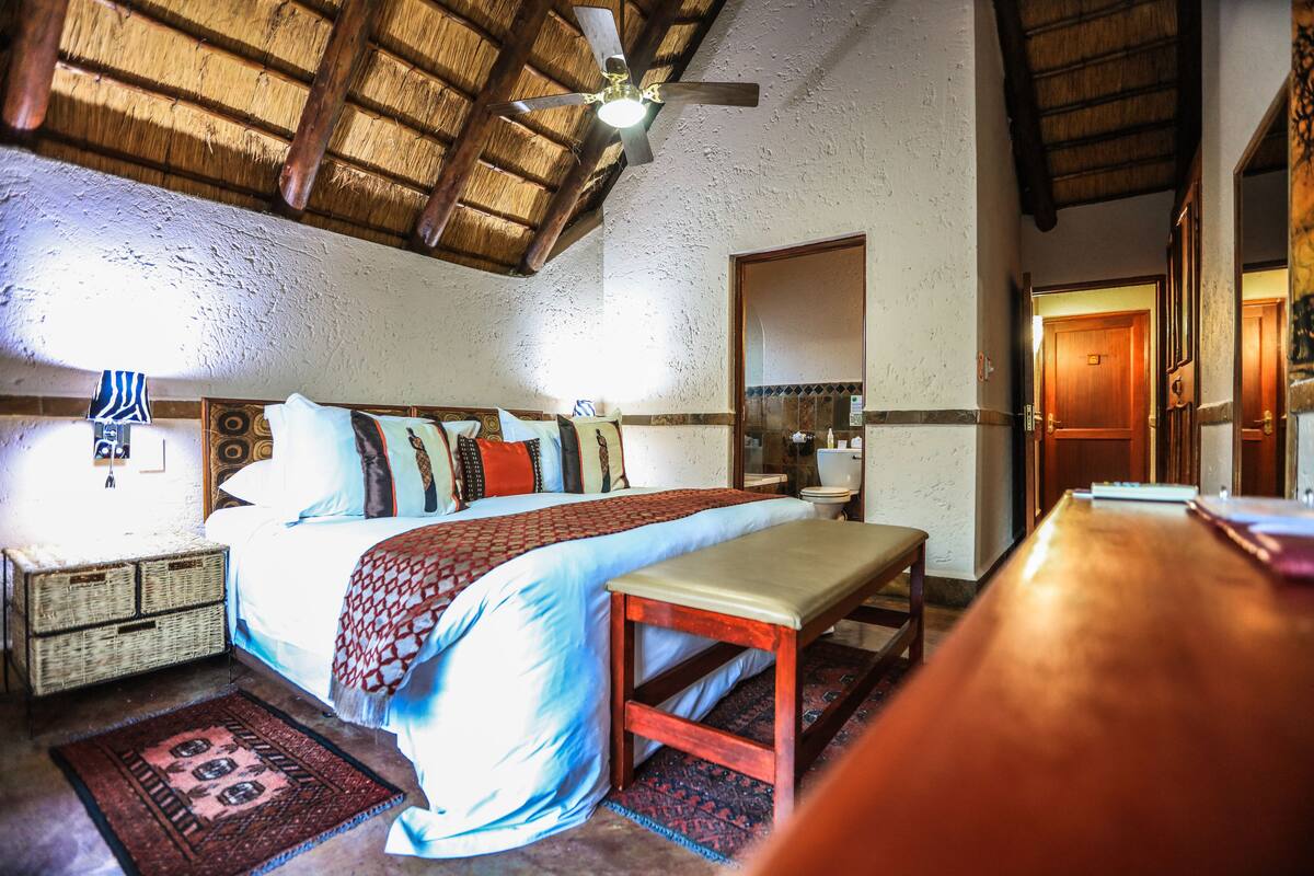 Ein Schlafzimmer mit einem Bett, einem Holzkopfende, Nachttischen, einer Bank, einem Deckenventilator und einer Holztür.