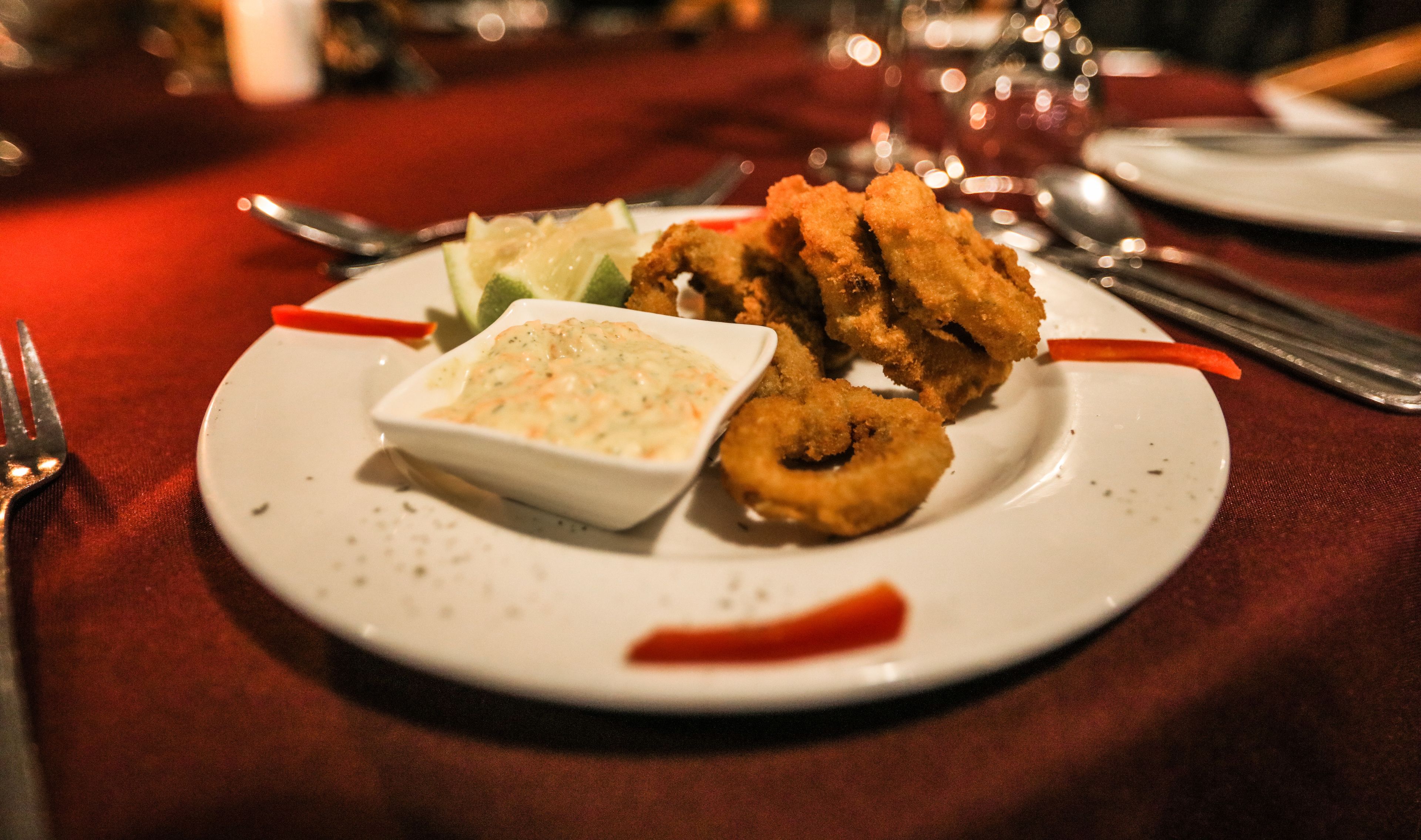 A plate with fried food, a small bowl of sauce, and a red garnish on a tablecloth.
