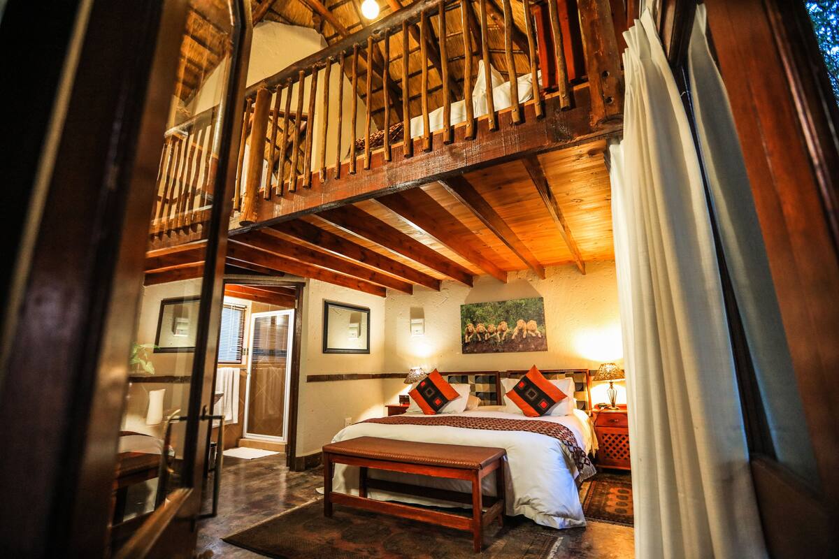 Ein Schlafzimmer mit einem großen Bett, Holzbalken an der Decke, einem Balkon und Blick ins Freie.