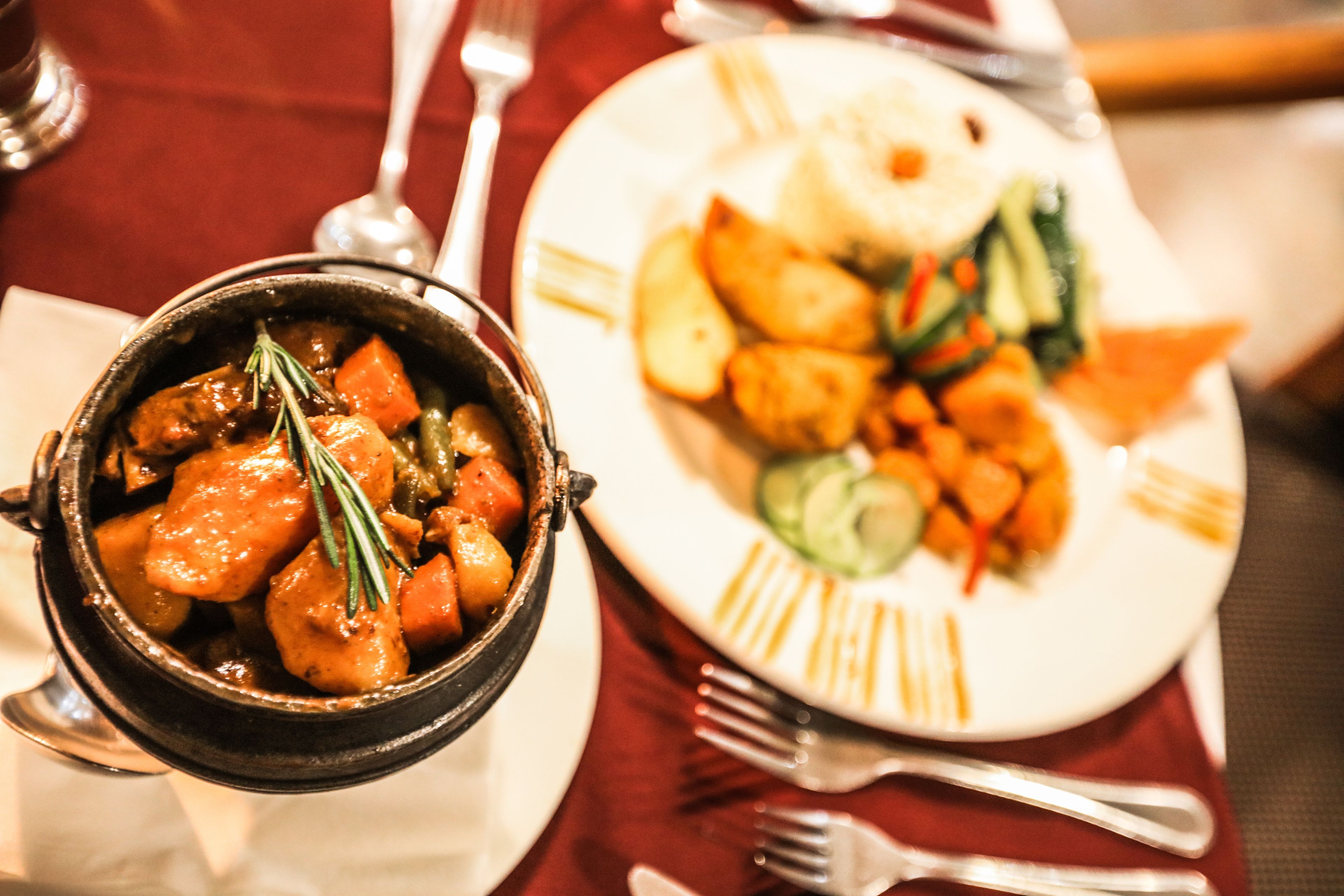 Une table à manger avec un bol de ragoût et une assiette de nourriture comprenant des pommes de terre et des légumes.