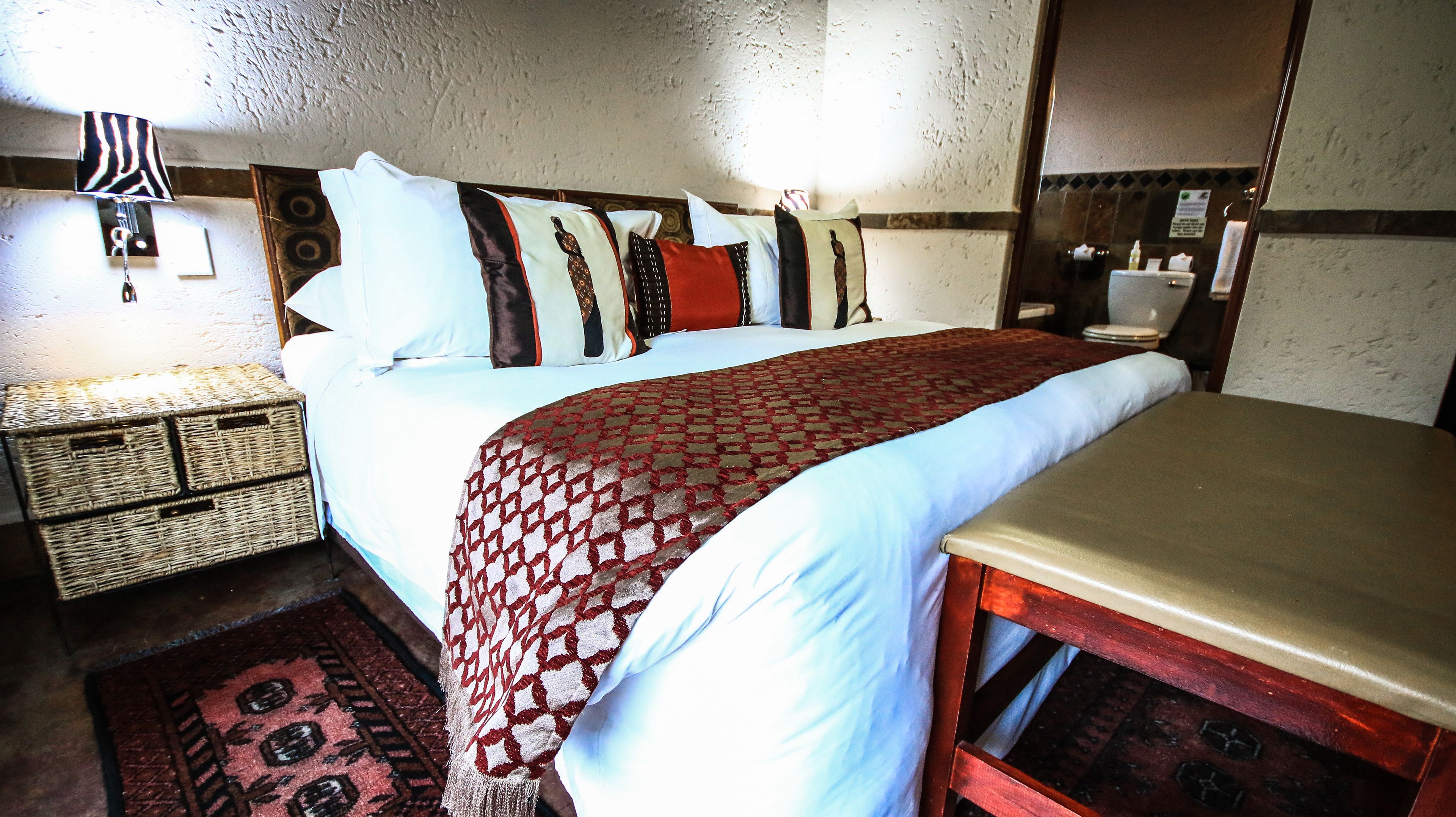 Ein Hotelzimmer mit Bett, Nachttisch, Lampe, Spiegel und kleinem Teppich.