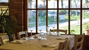 A dining table set for four with clear glassware and a view of a garden through large windows.