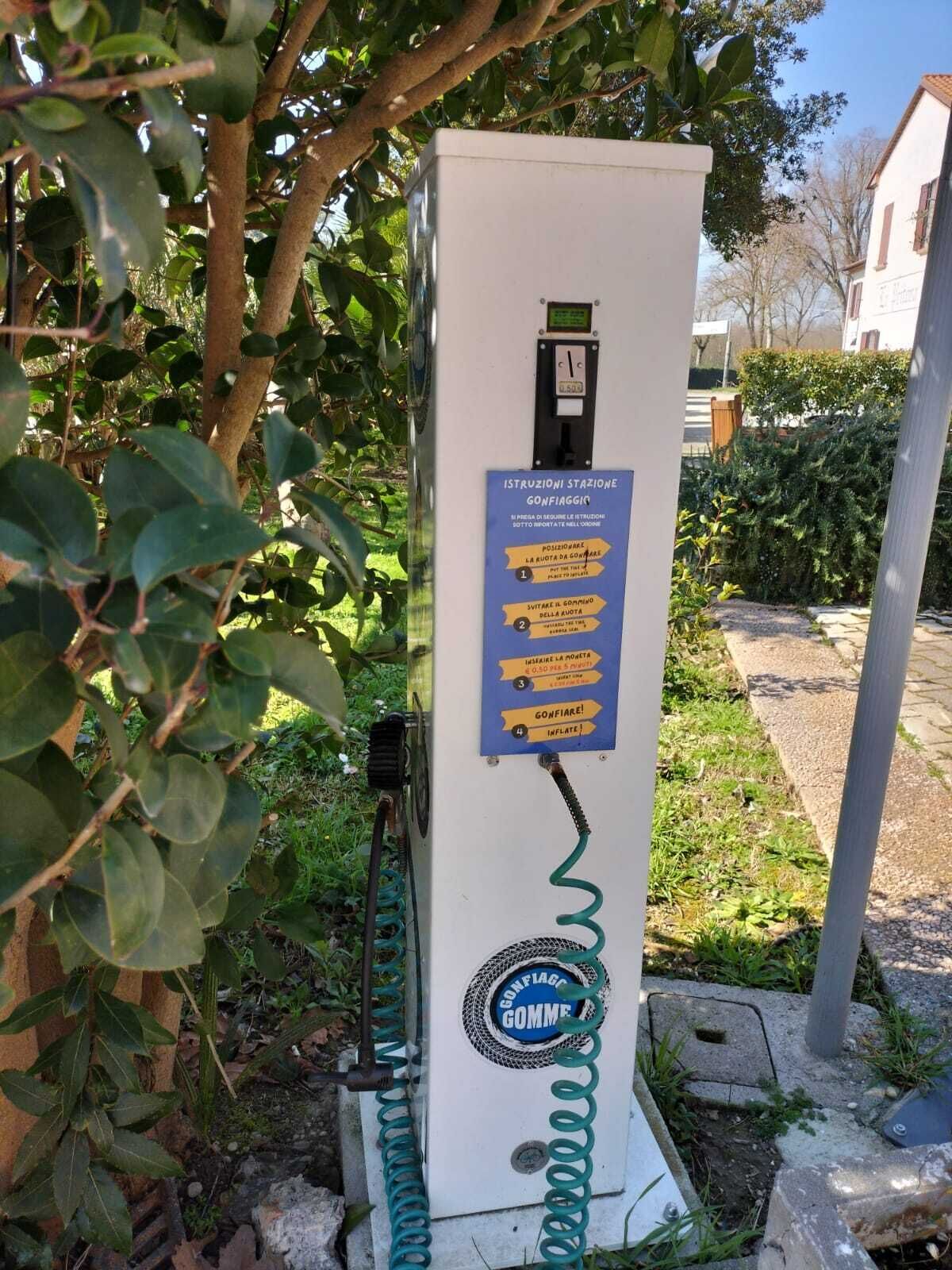 A public electric vehicle charging station with instructions in Italian, surrounded by greenery.
