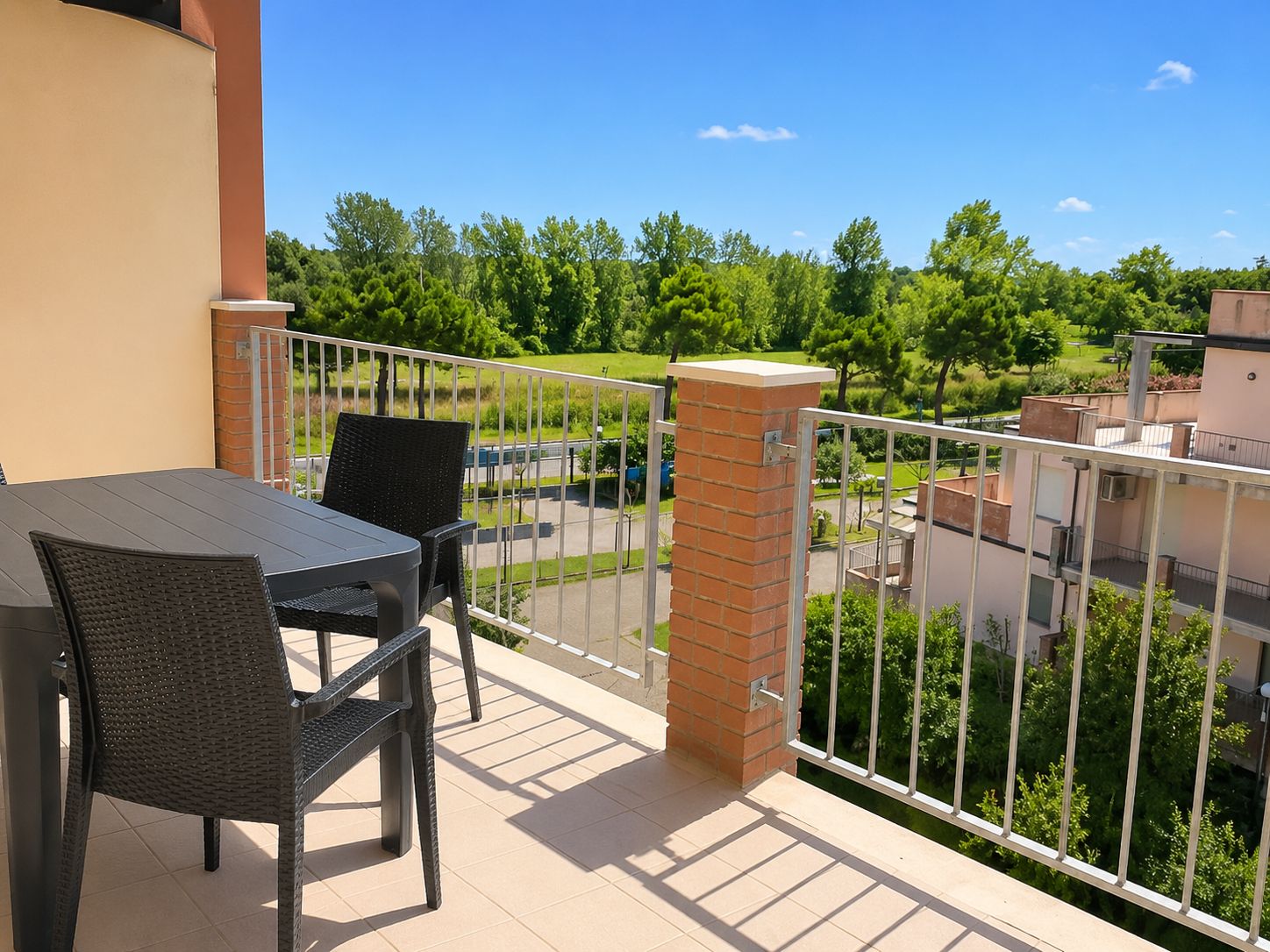 Un balcone con tavolo e sedie, un pilastro in mattoni e vista su un paesaggio verde e edifici.