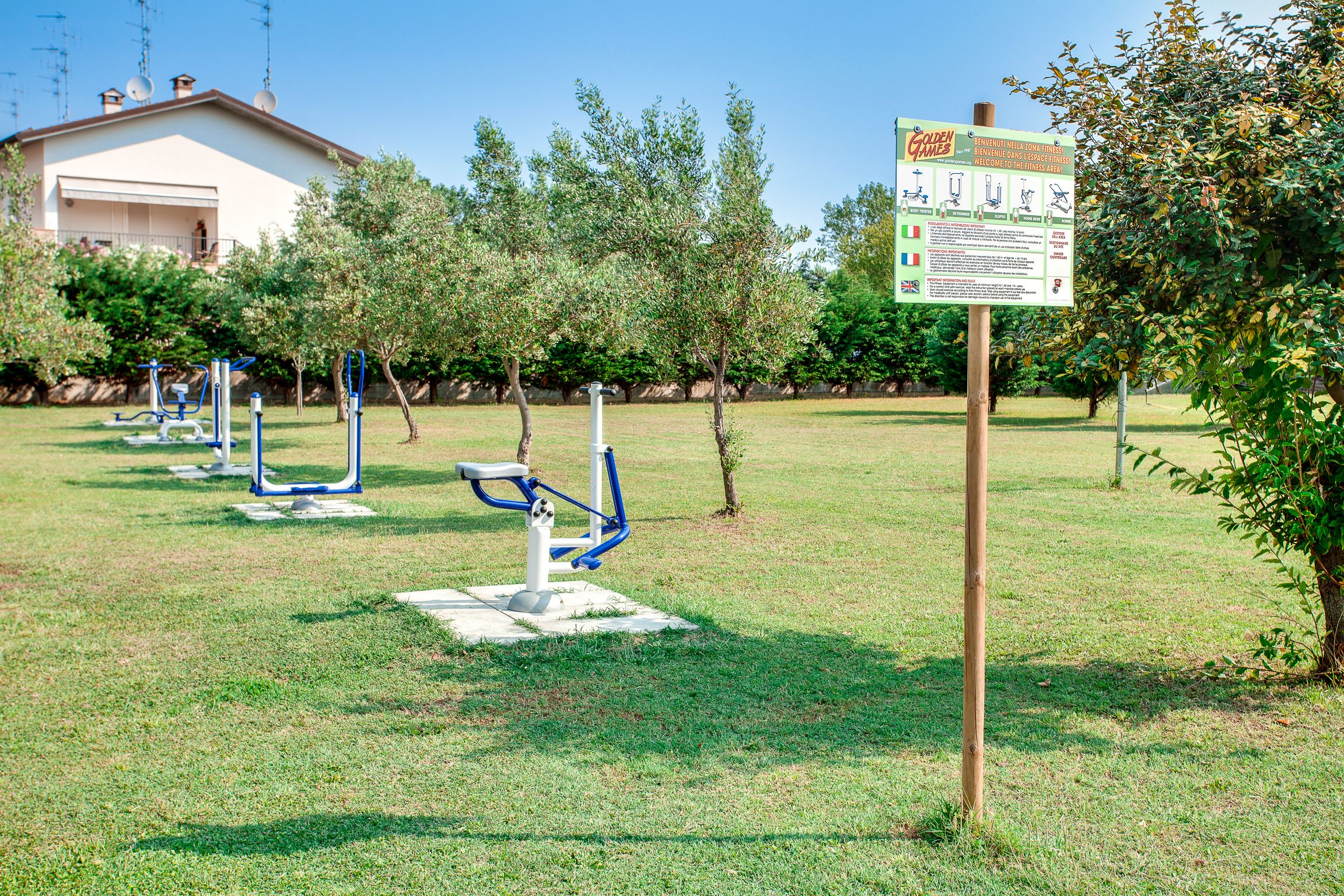 Outdoor exercise equipment in a grassy area with a signboard.