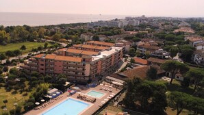 An aerial view of a residential area with a large building featuring multiple balconies, a swimming pool, and a sports field.
