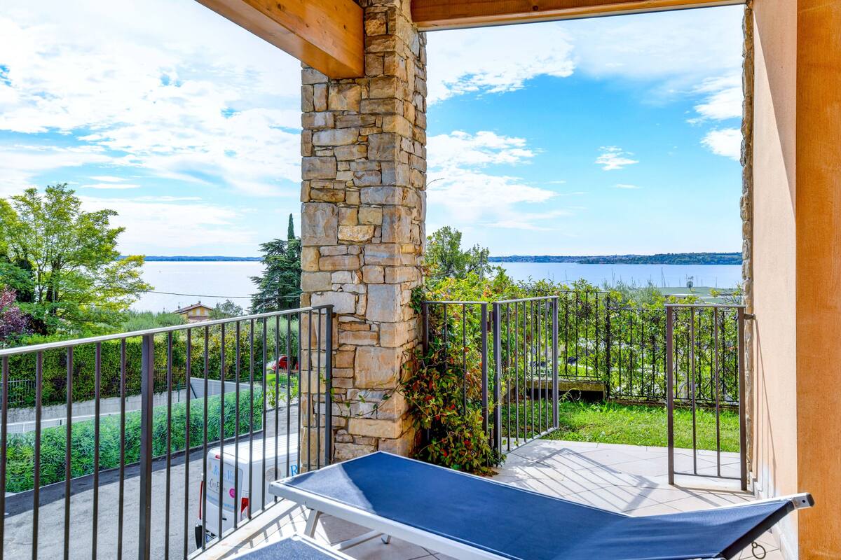 A balcony with a stone pillar, a metal railing, and a view of a lake.