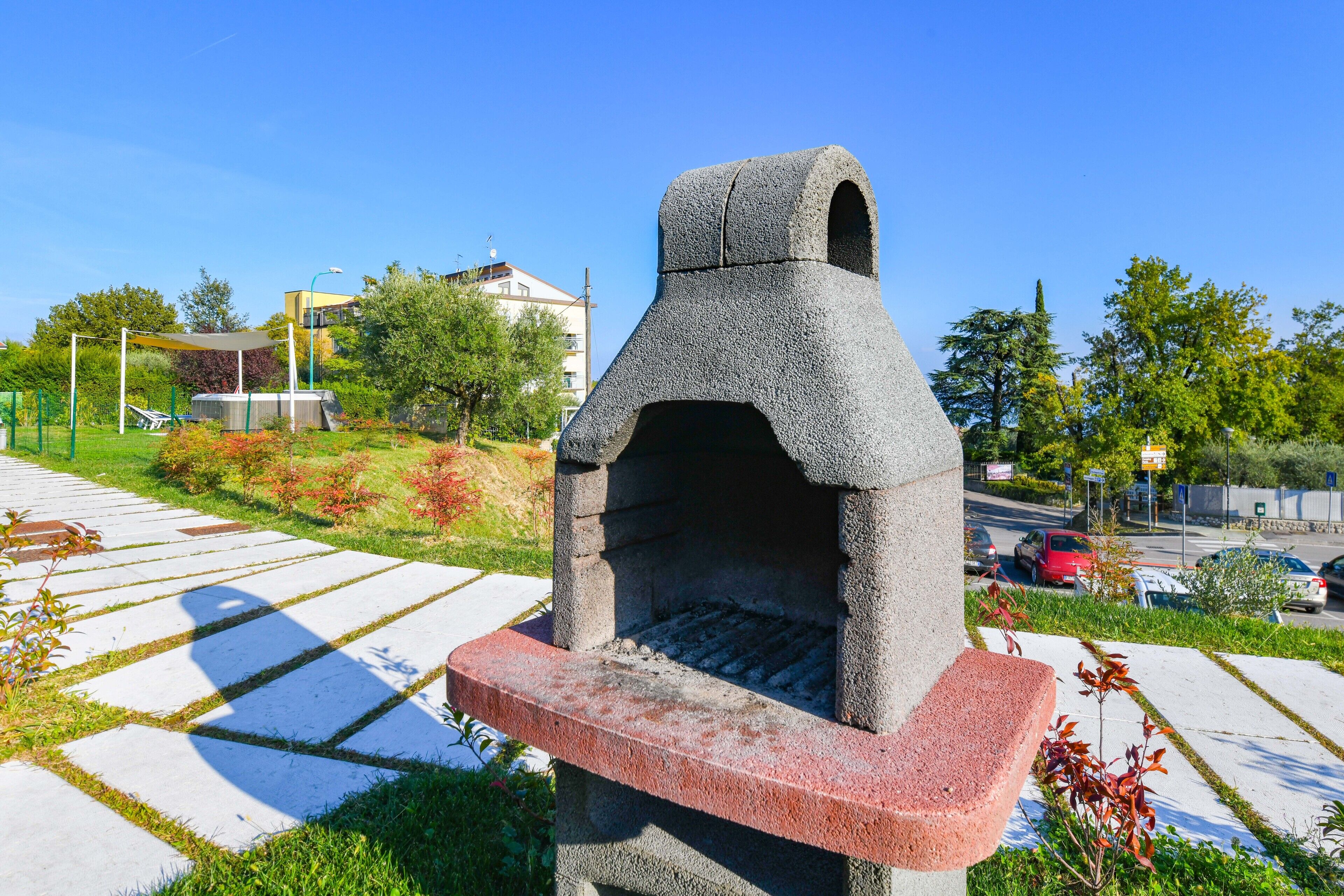 Una struttura esterna in pietra, probabilmente una zona barbecue, con un vialetto lastricato in primo piano e edifici sullo sfondo.
