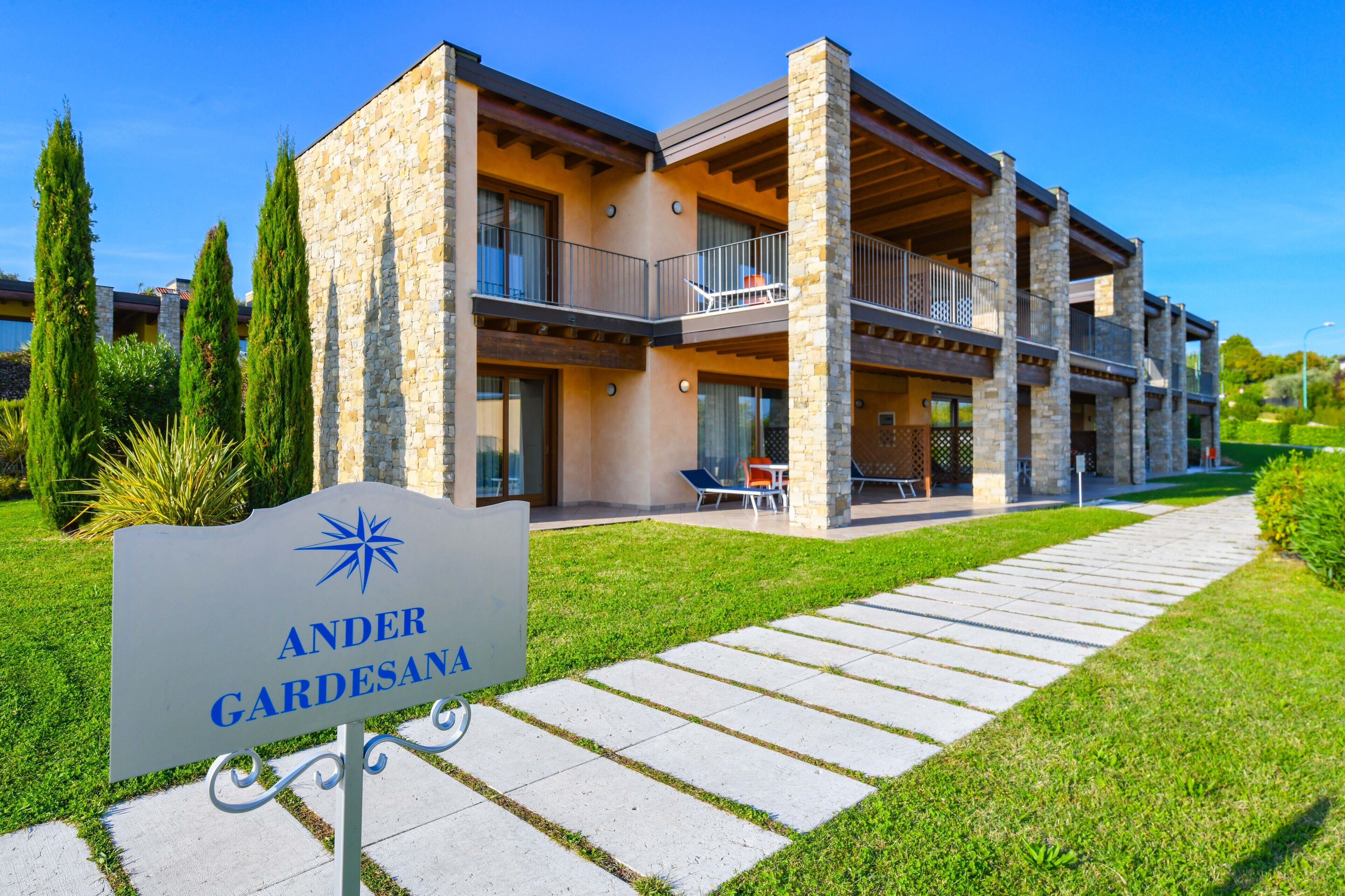 A modern hotel with a stone facade, multiple balconies, and a well-maintained lawn.