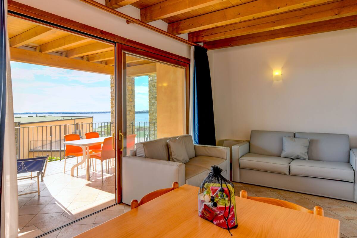 A modern living room with a wooden ceiling, a sofa, a table, and a balcony with a view of the sea.