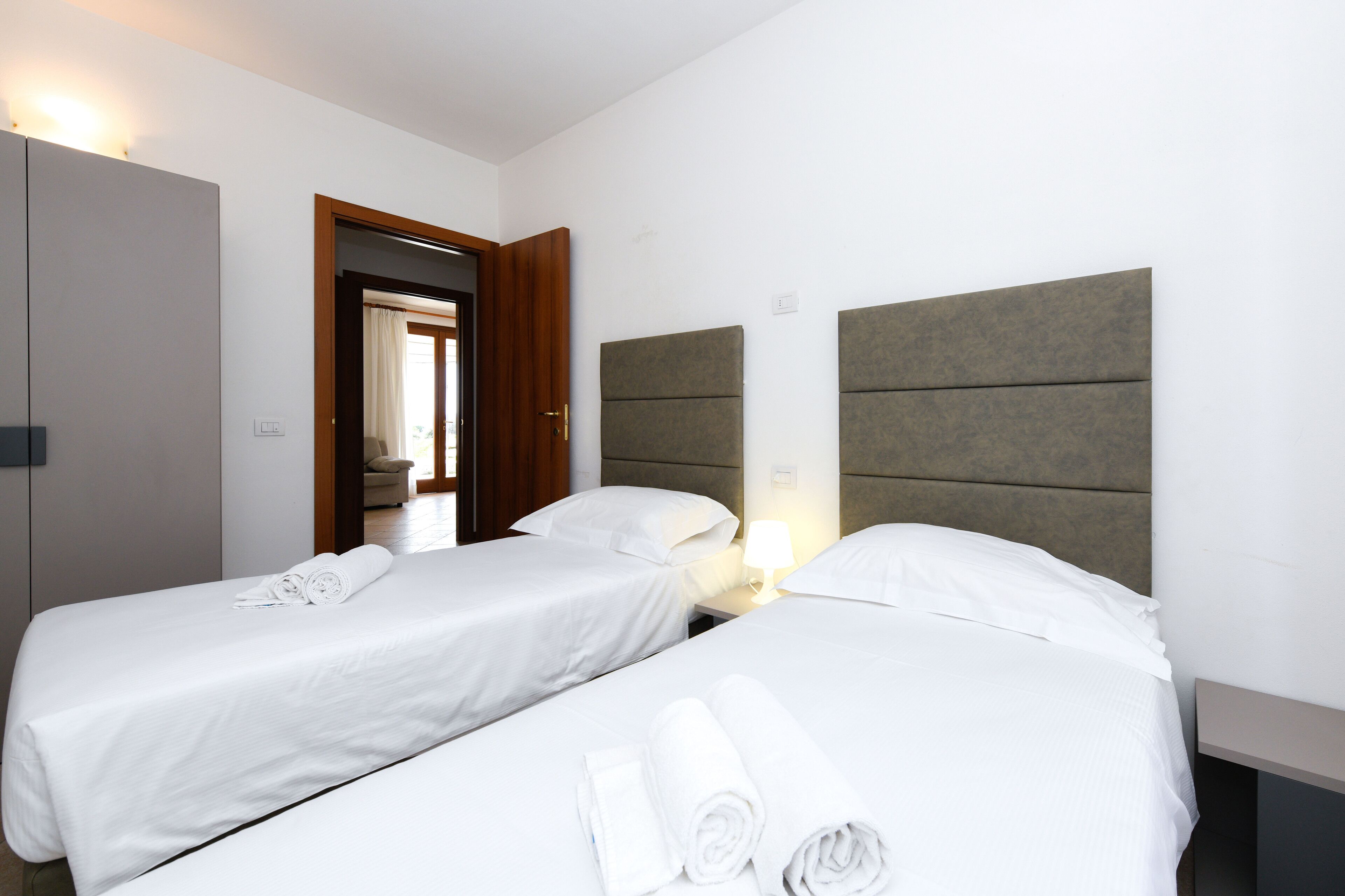 Ein Hotelzimmer mit zwei Einzelbetten, einer Holztür und einem Nachttisch mit Lampe.