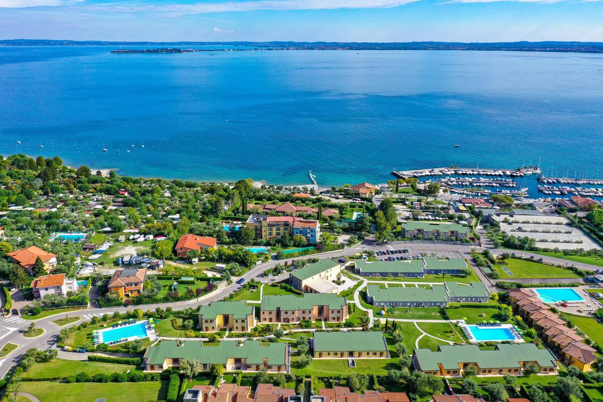 An aerial view of a coastal town with a marina, residential buildings, and a large swimming pool complex.