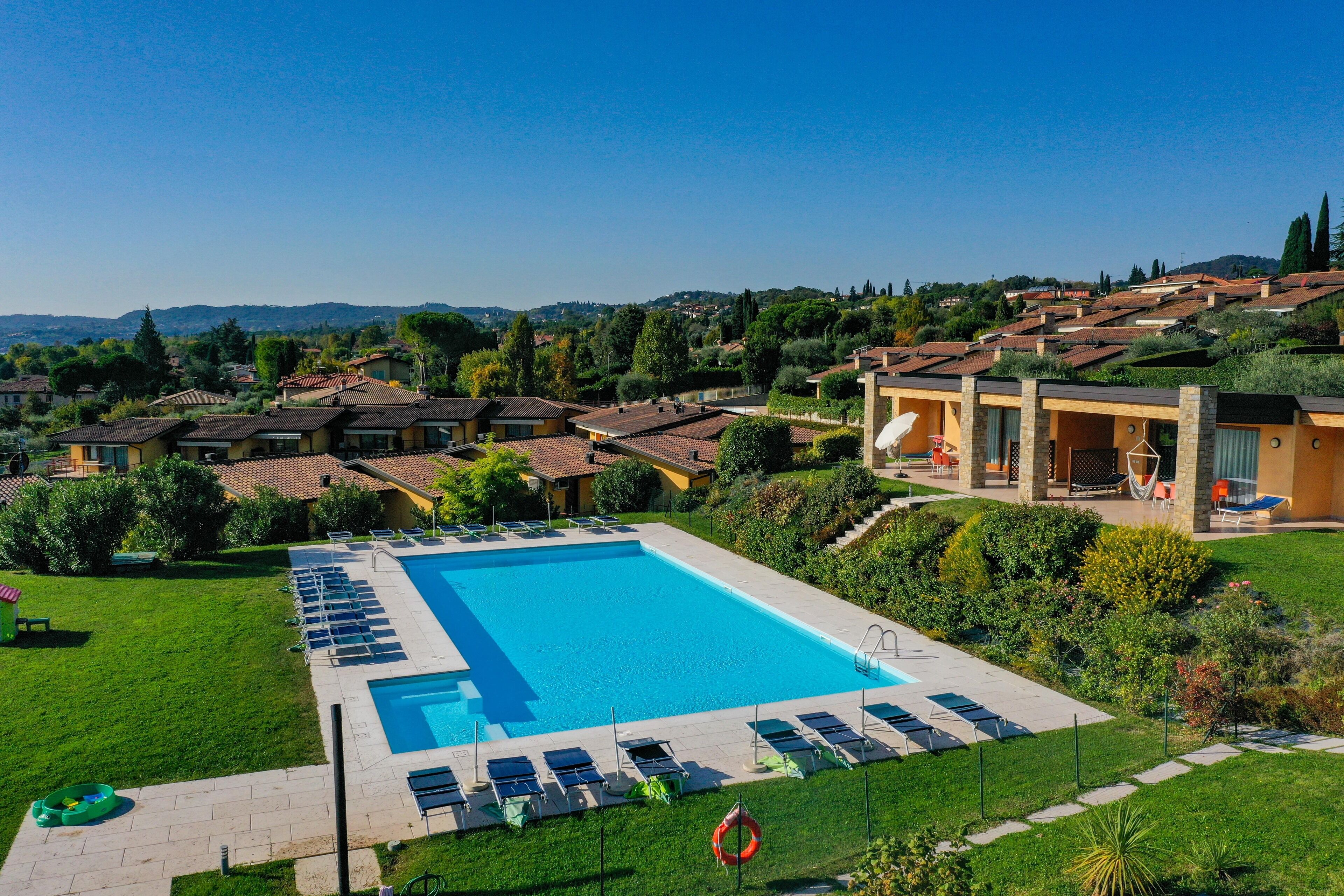 Una piscina con sillas de descanso, un área verde y vistas de casas circundantes.