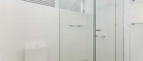 Un baño moderno con cabina de ducha de vidrio, azulejos blancos y un inodoro.