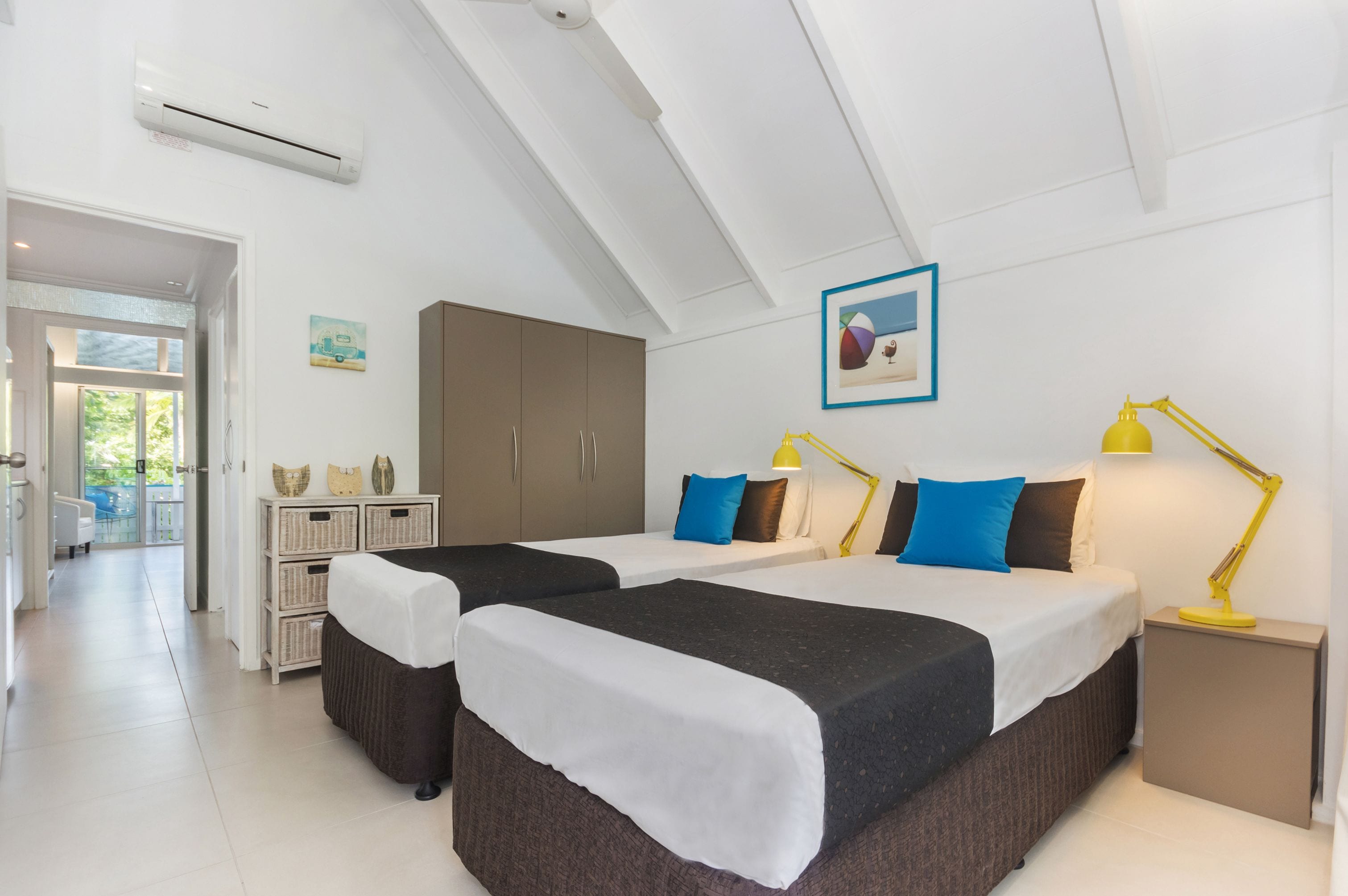 A modern hotel room with two beds, a wardrobe, a desk, and a balcony.