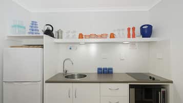 Una cucina compatta con frigorifero, lavandino, forno a microonde e un piano di lavoro con diversi oggetti.