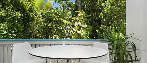 A round table with two white chairs, a white fence, and various green plants in the background.