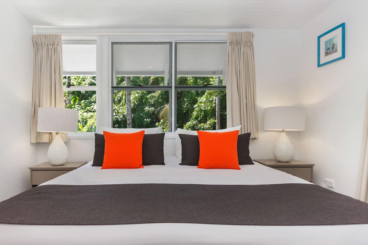 A hotel room with a large bed, two nightstands, a window with curtains, and a framed picture on the wall.