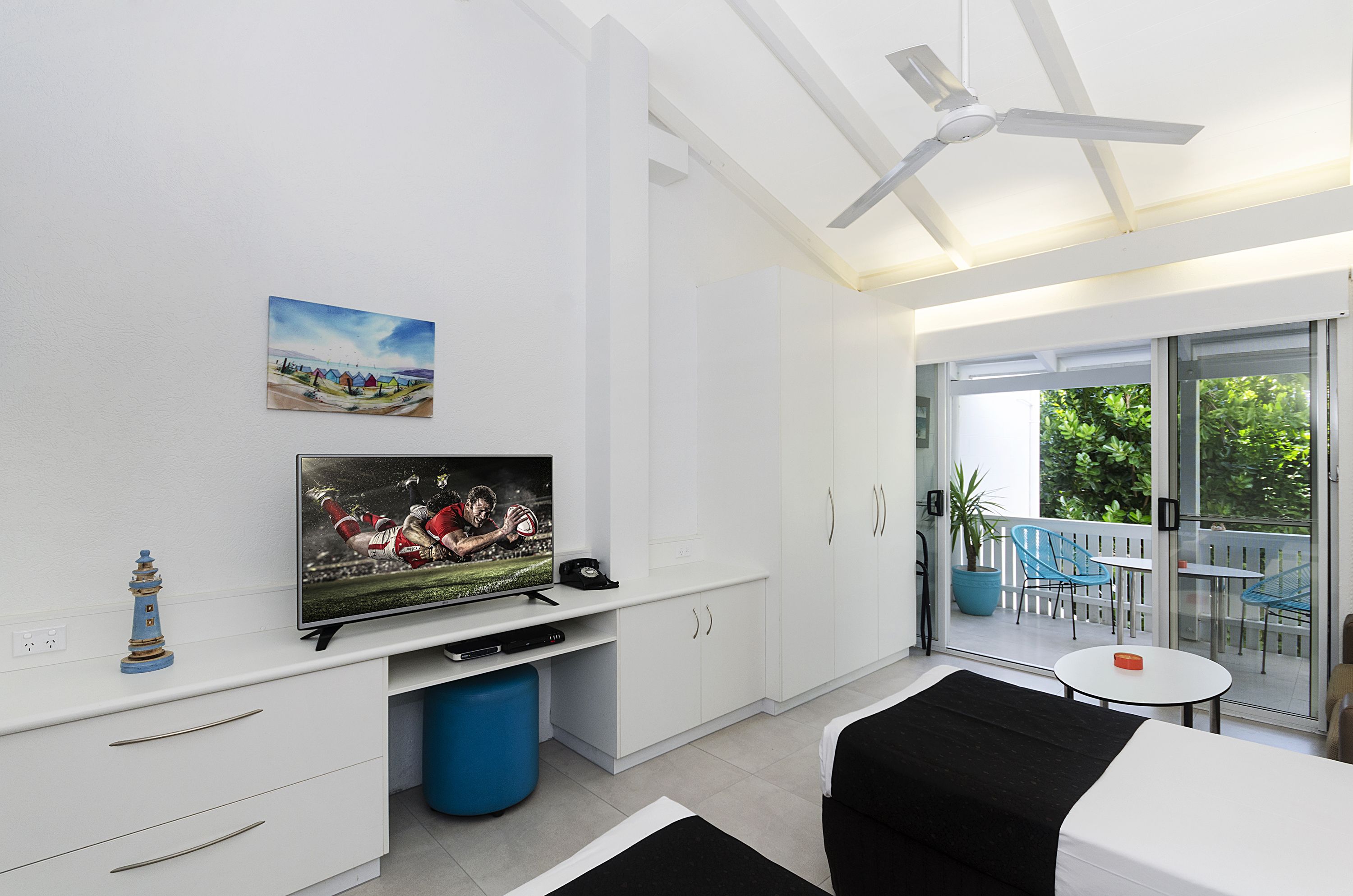 Een moderne woonkamer met een flatscreen televisie, een plafondventilator en een balkon met tuinmeubilair.