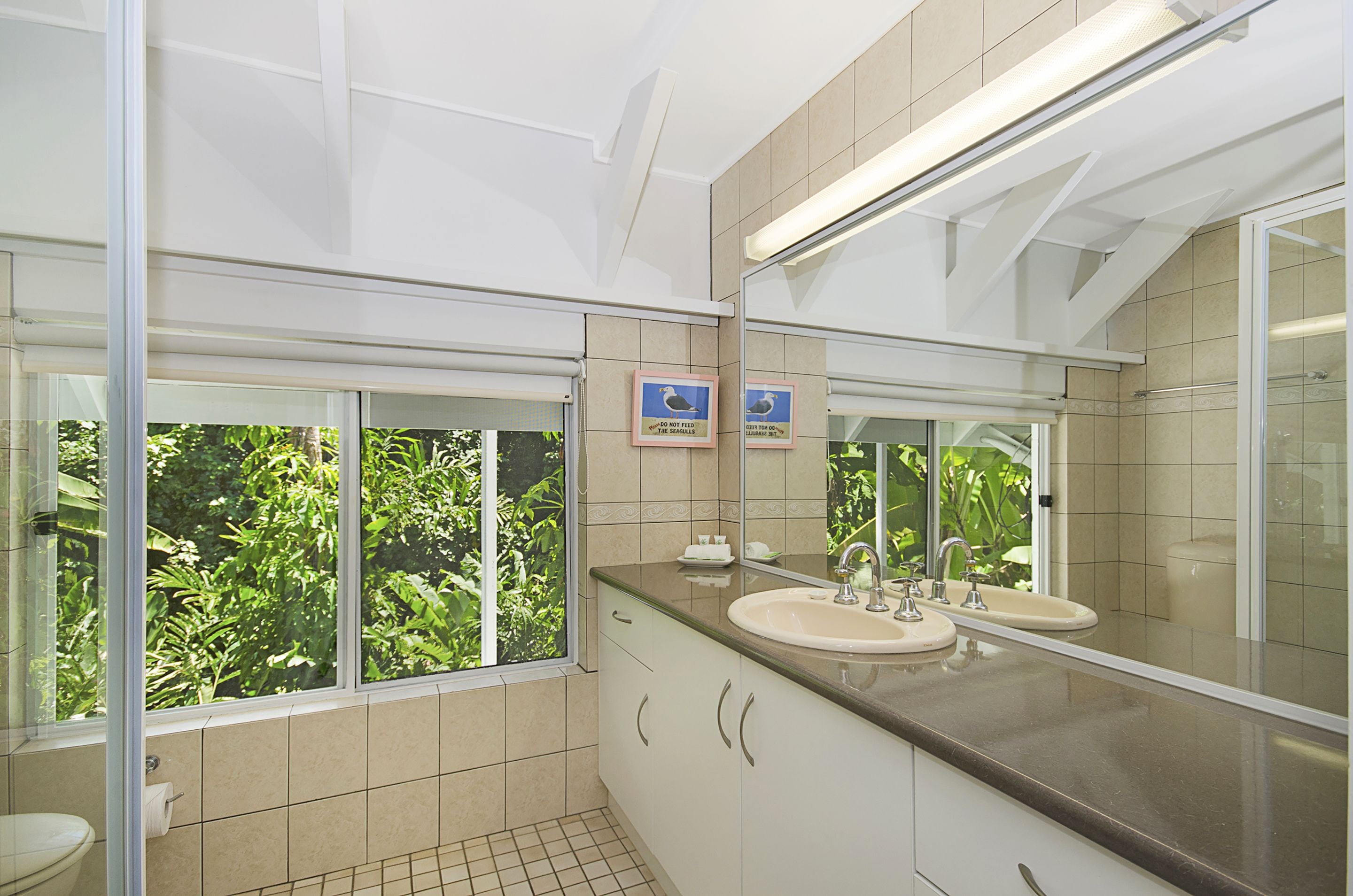 Een moderne badkamer met twee wastafels, een grote spiegel en een raam met uitzicht op groen.