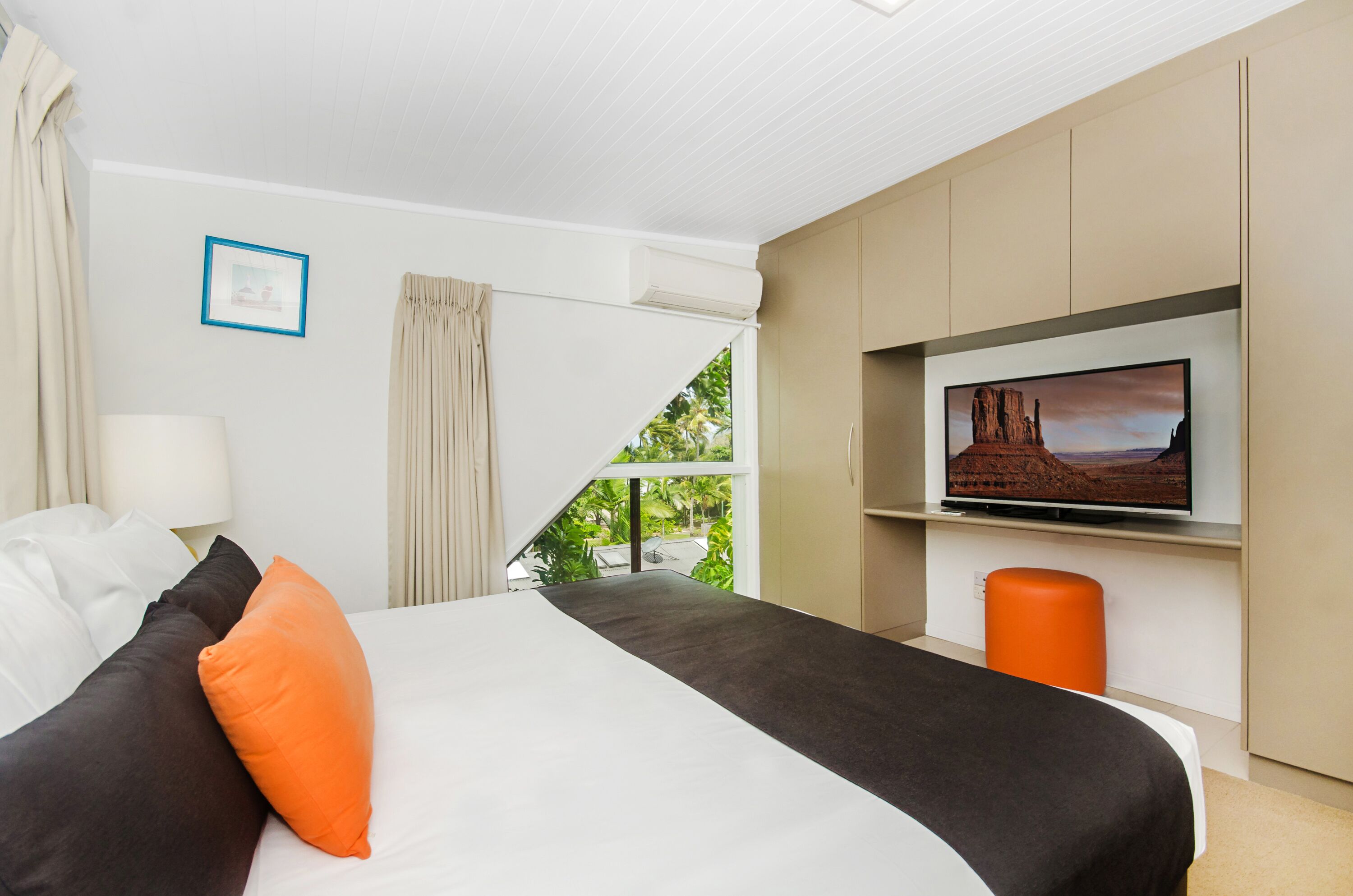 Camera d'albergo con un letto, una televisione, una finestra con tende e vista sul verde.