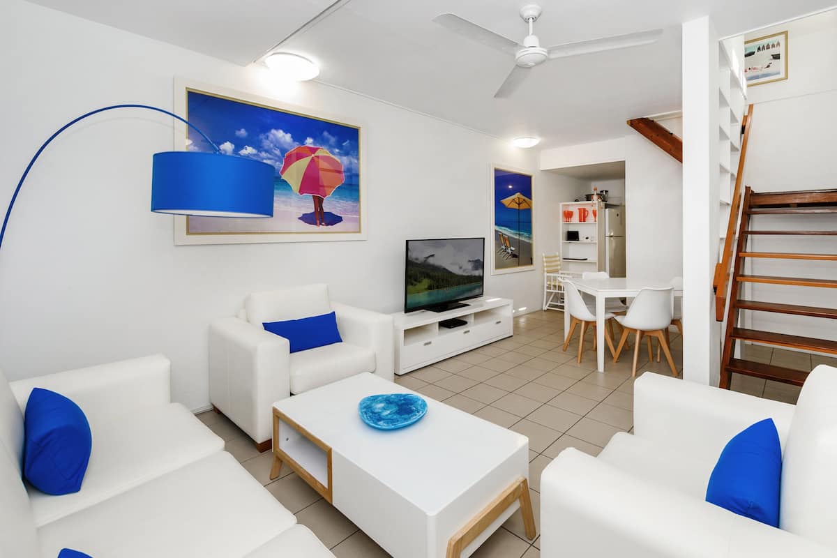 A modern living room with white sofas, a coffee table, a TV, and artwork on the walls.