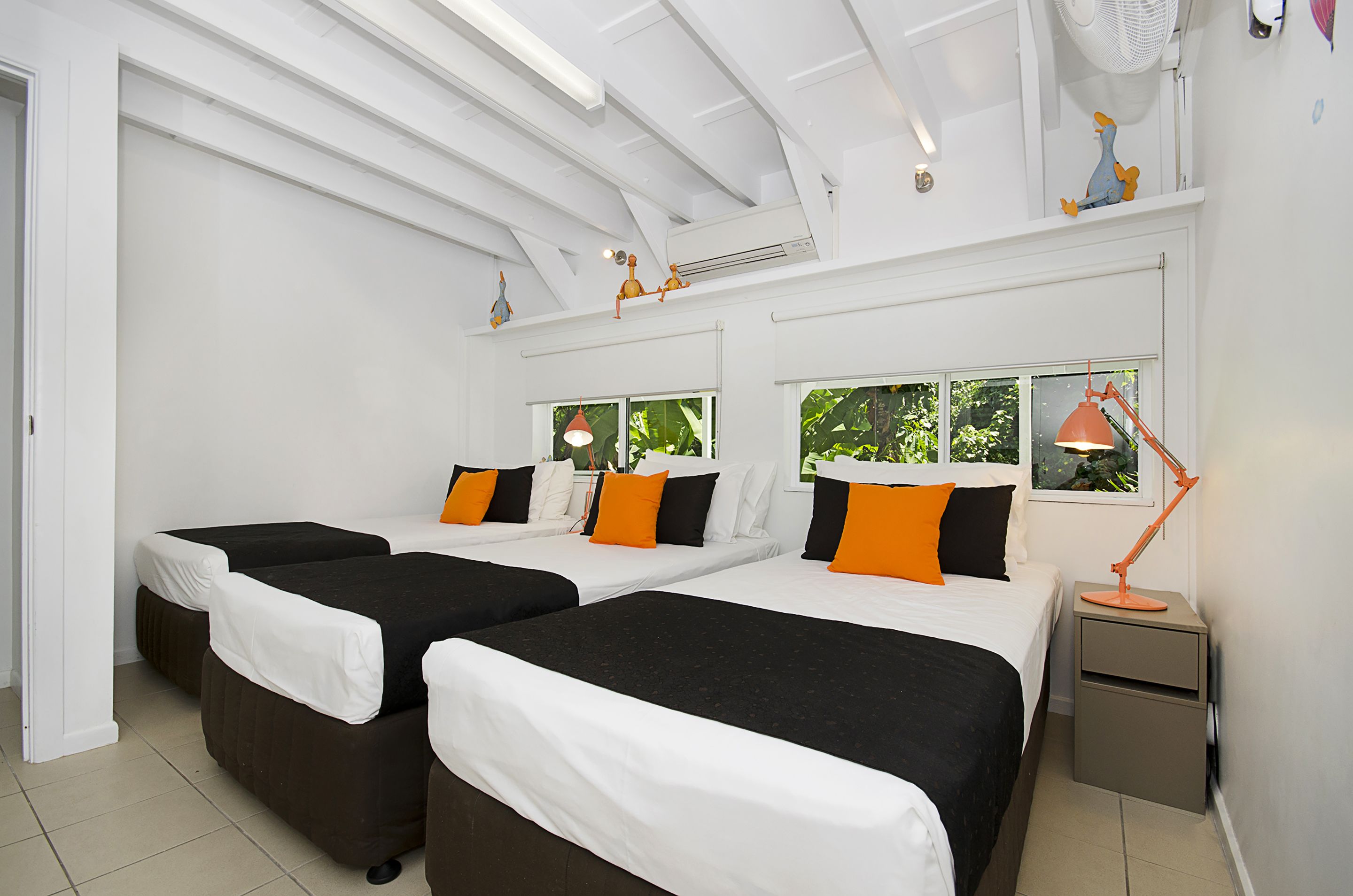 A hotel room with two beds, a nightstand, a desk, a chair, and a window with a view of greenery.