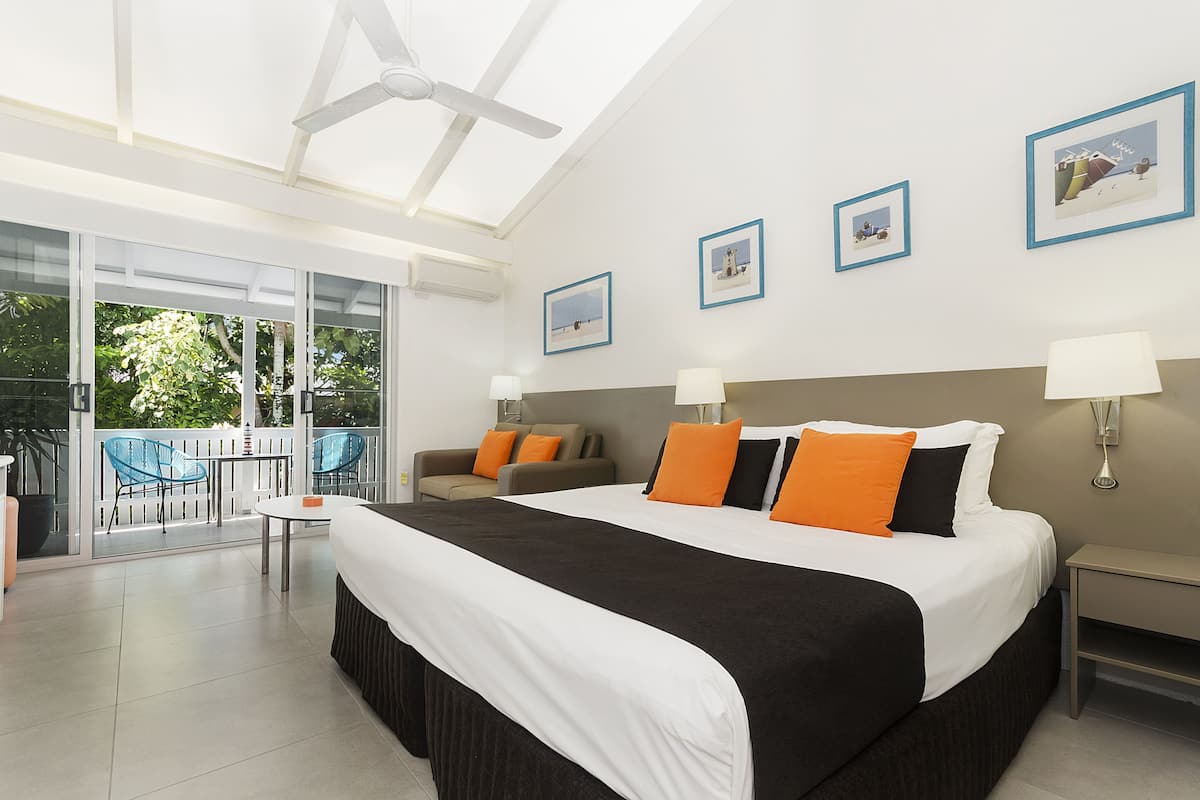 A modern hotel room with a large bed, two bedside tables, a ceiling fan, and a balcony with outdoor furniture.