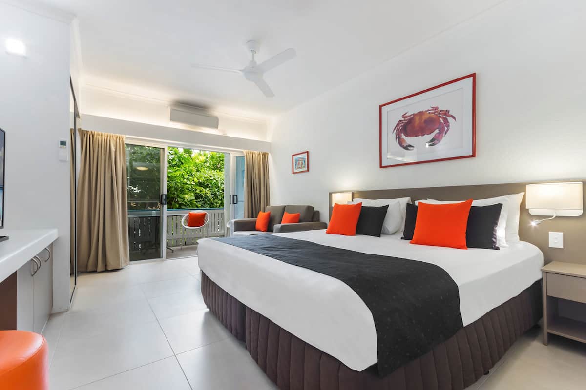 A hotel room with a large bed, a desk, a chair, a balcony with curtains, and a ceiling fan.