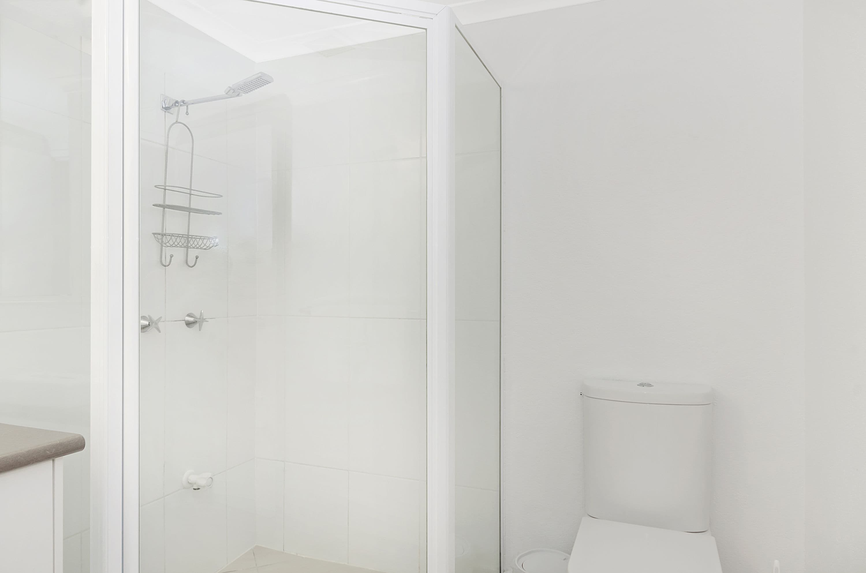 A modern bathroom with a glass-enclosed shower, a toilet, and a towel rack.