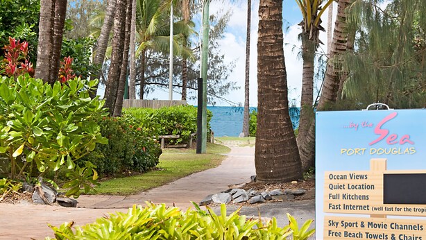 A sign for a hotel with amenities including ocean views, a quiet location, full kitchens, fast internet, sky sport & movie channels, free beach towels & chairs, and a heated pool. - By The Sea Port Douglas (Port Douglas)