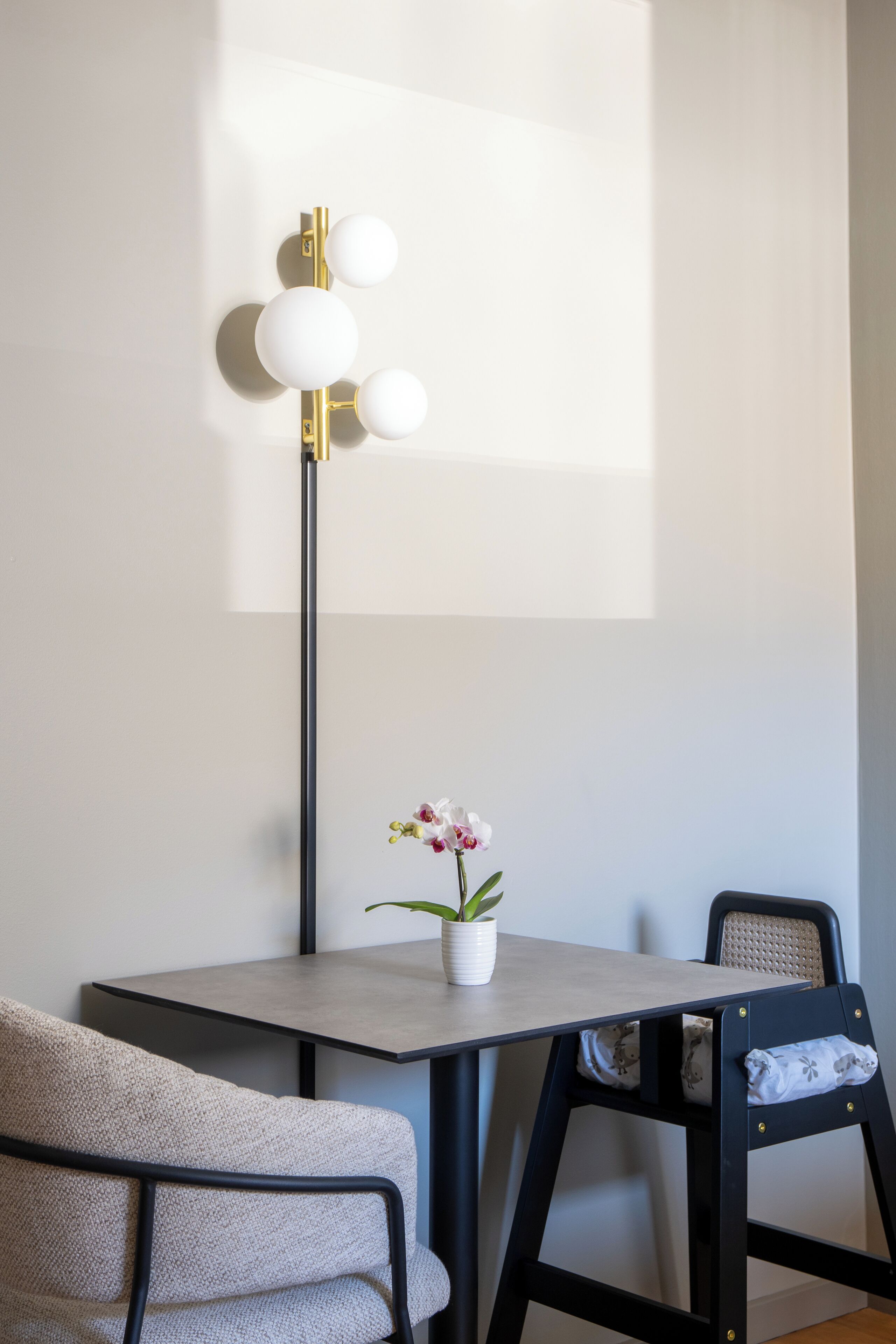 A modern dining area with a minimalist table, a black metal chair, and a floor lamp with three spherical lights.