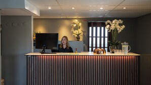 A reception desk with a modern design, a flat-screen TV, and a potted plant. - VICI Hotels Linköping (Linkoping)