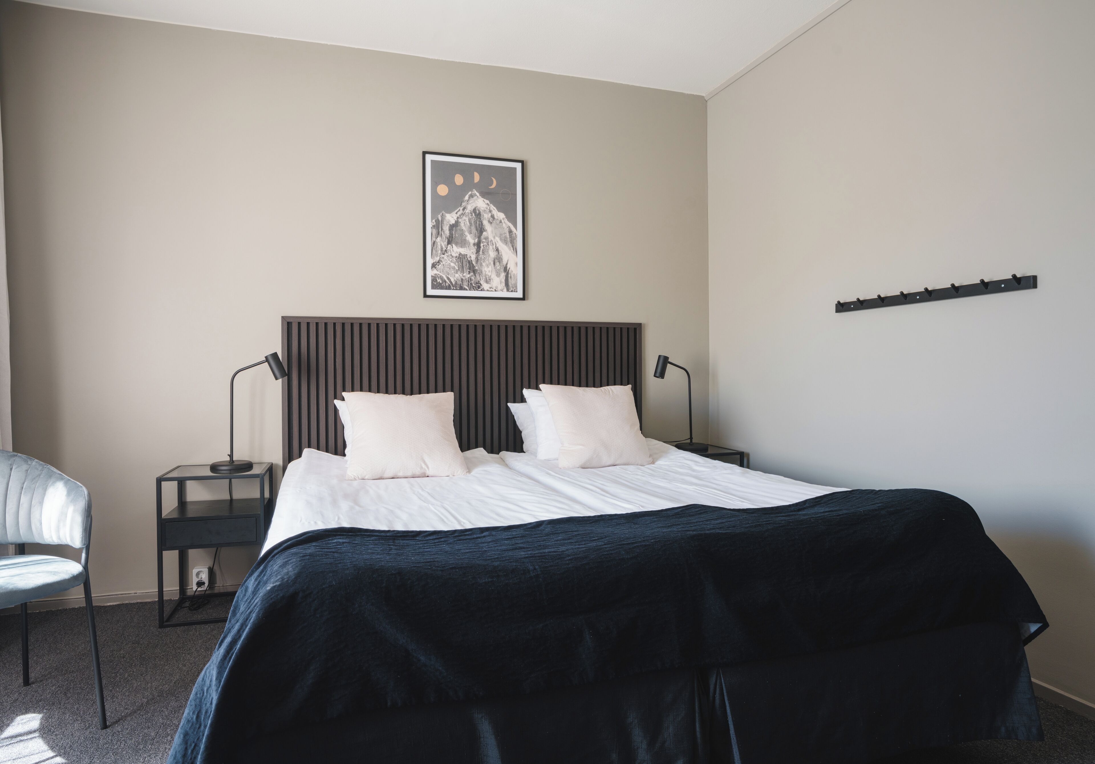 A modern bedroom with a bed, a bedside table, a chair, and a wall-mounted shelf.