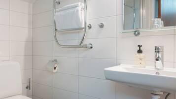 Un baño con inodoro blanco, un perchero, un lavabo con espejo y una botella de jabón para manos.